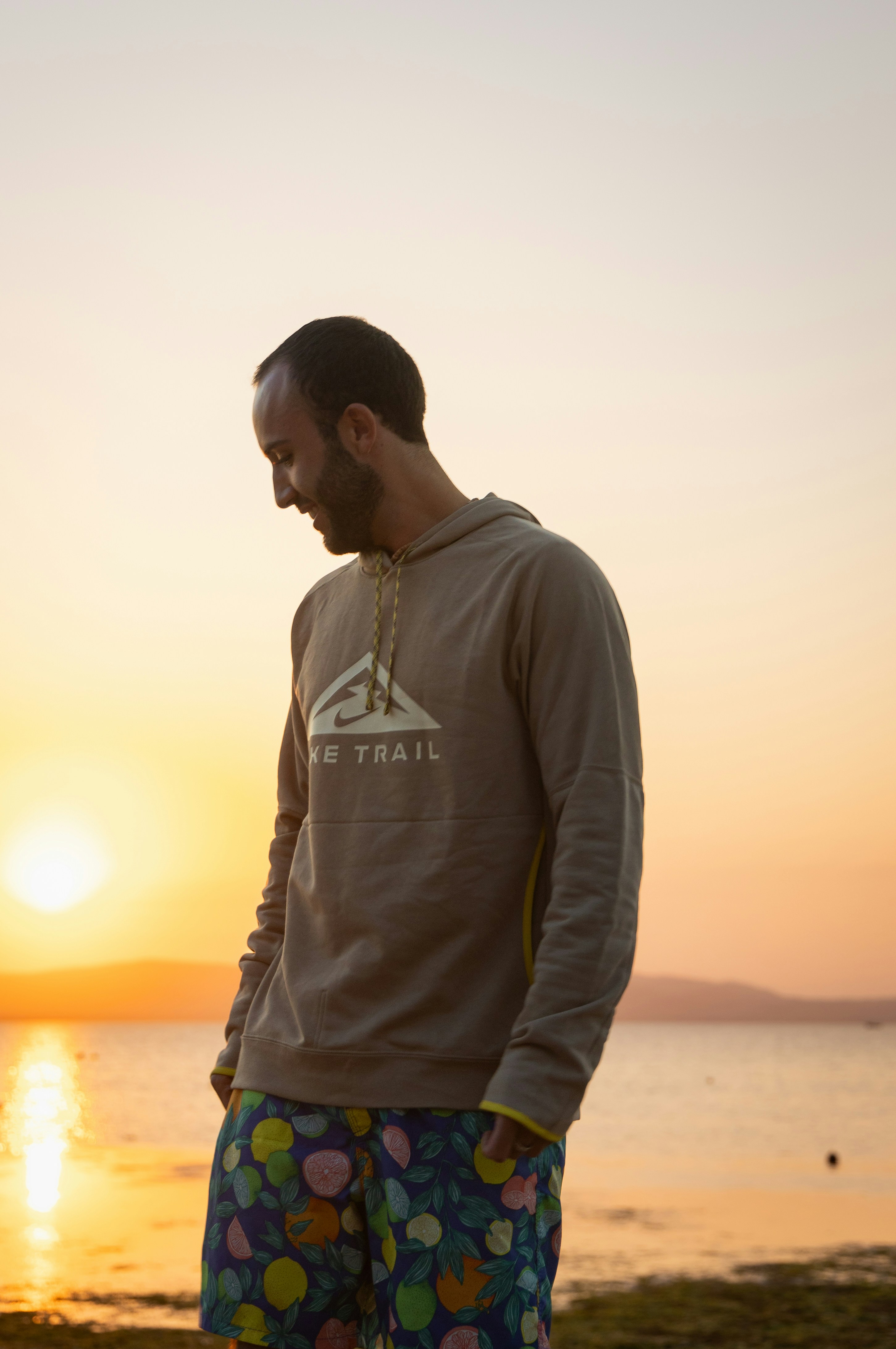 Mann im Hoodie am Meer bei Sonnenuntergang.