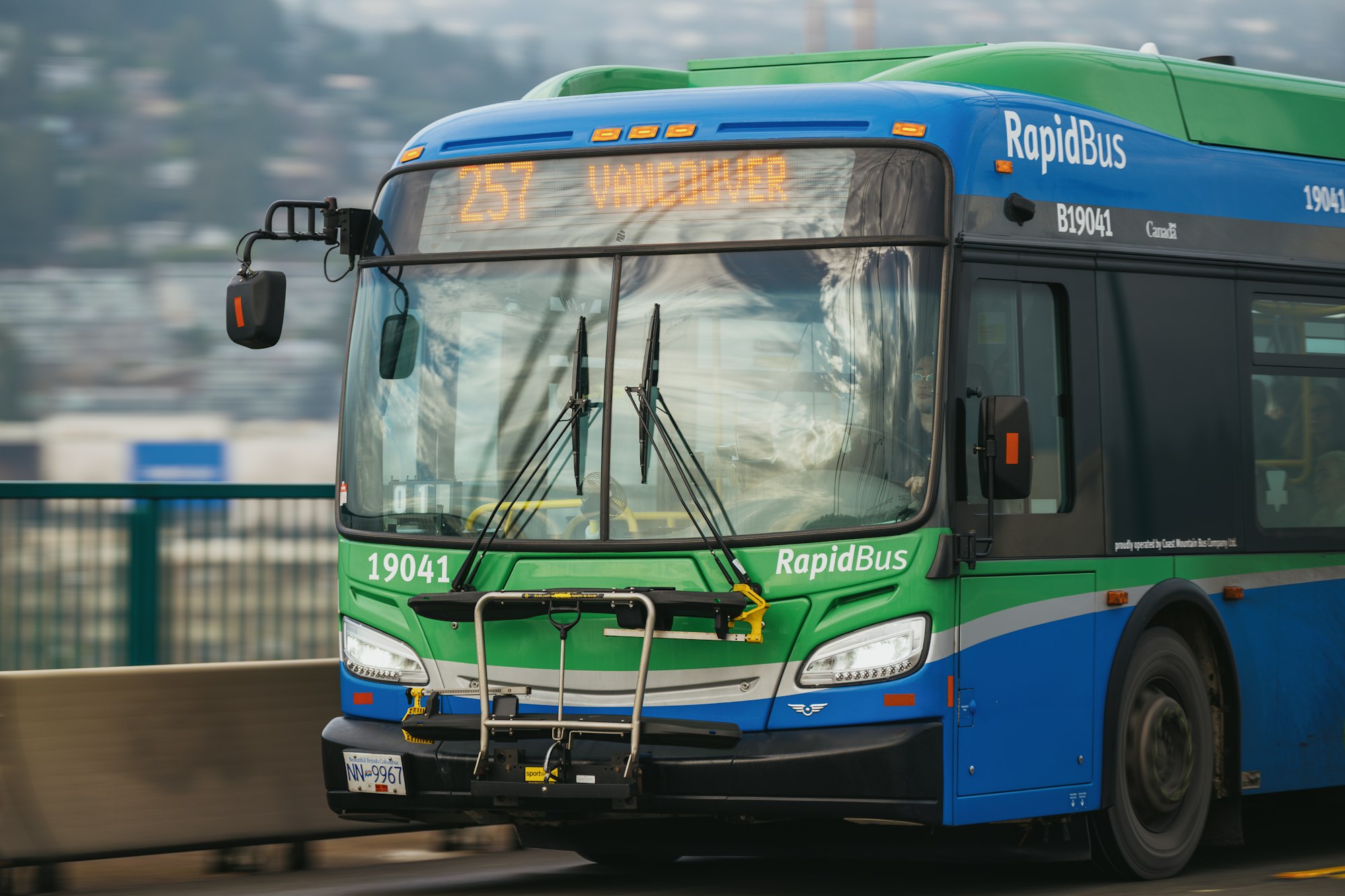 A blue and green rapidbus transit bus on a bridge.