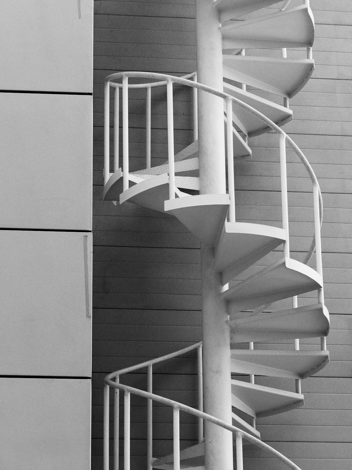 Close view of a white powder-coated steel spiral staircase against a building facade