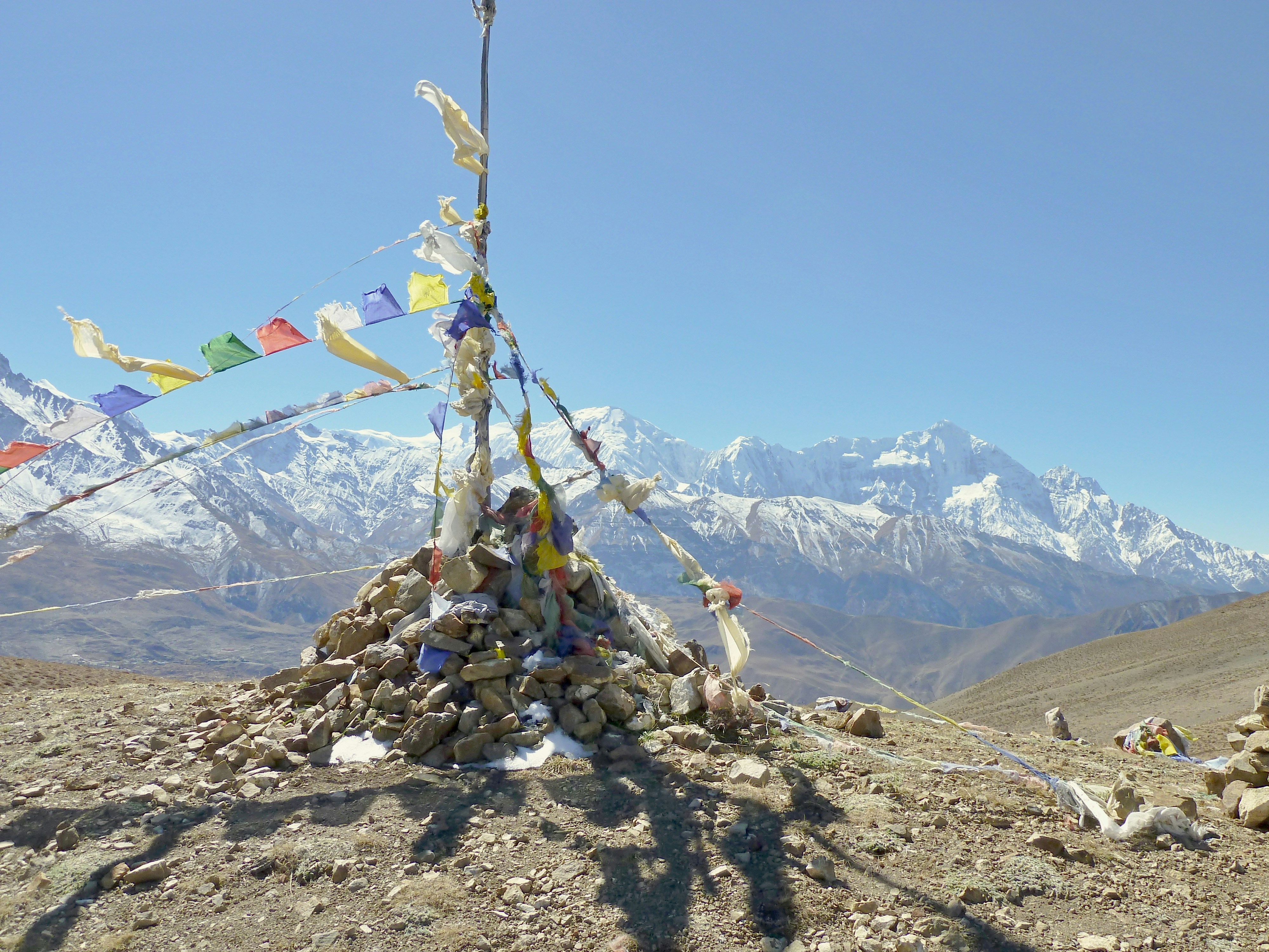 Des drapeaux de prière flottent sur un cairn entouré de montagnes enneigées derrière