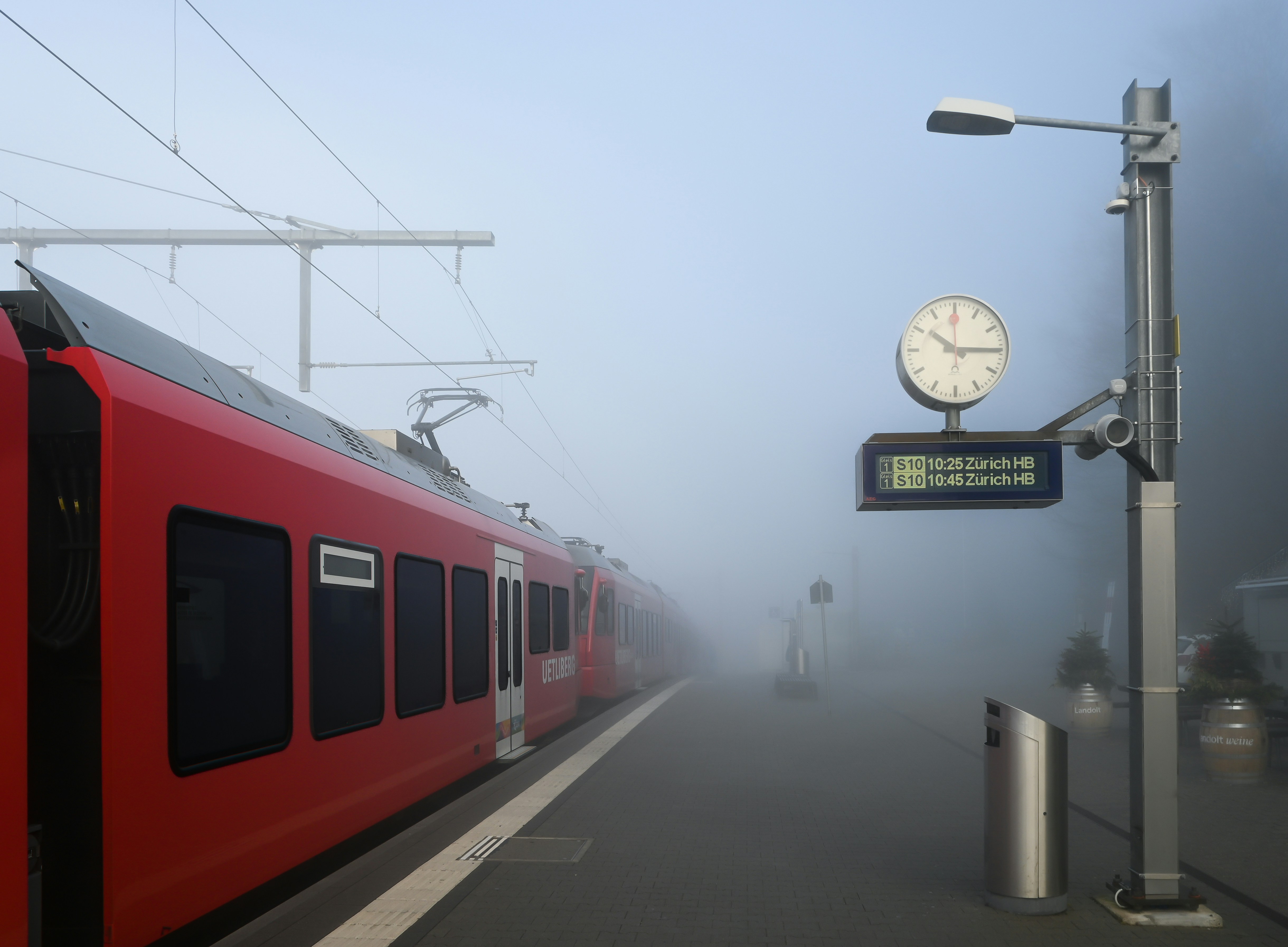 Red train at a foggy station with a clock.