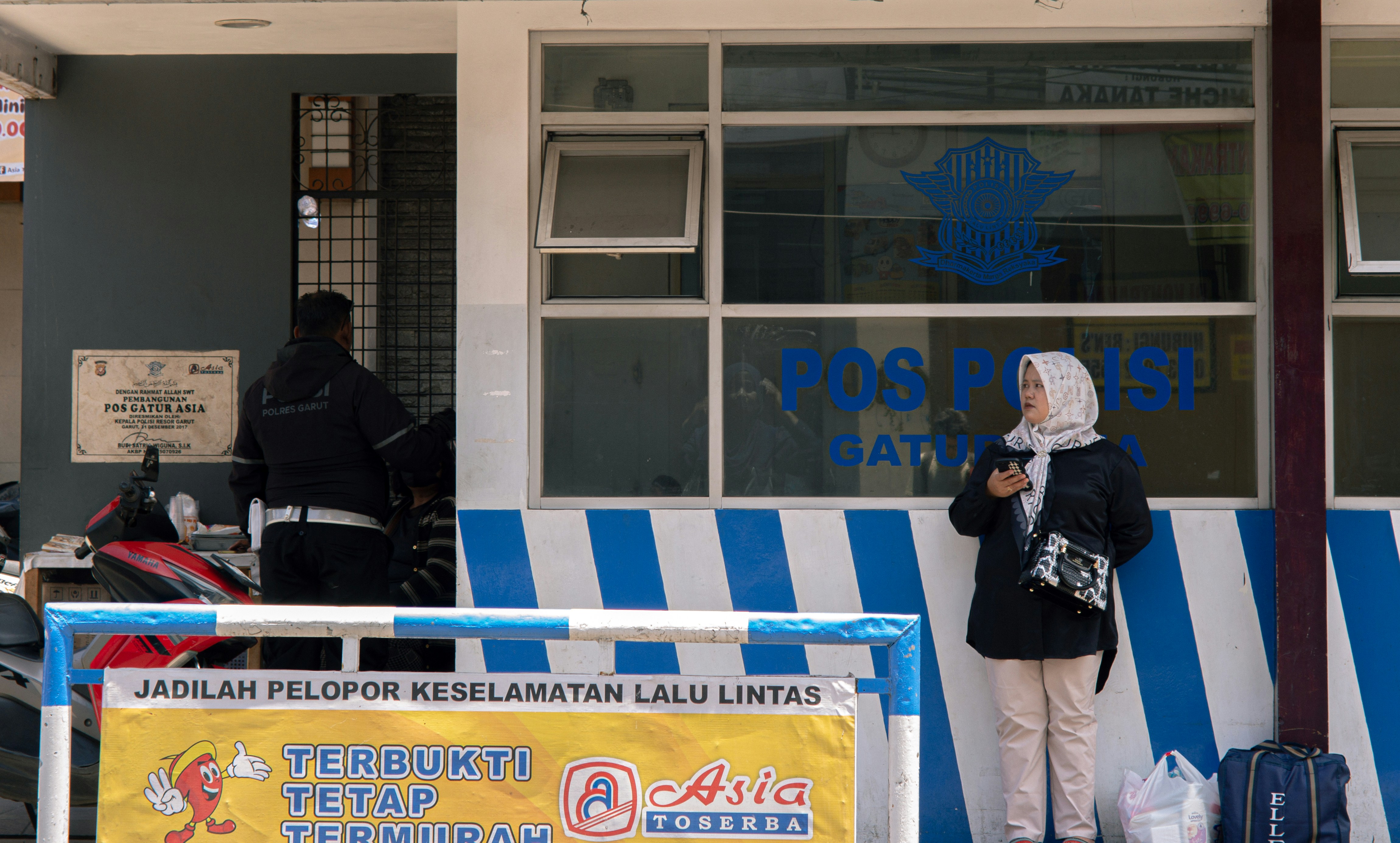 A police officer in uniform speaking to reporters outside a police station, with news cameras in the foreground.