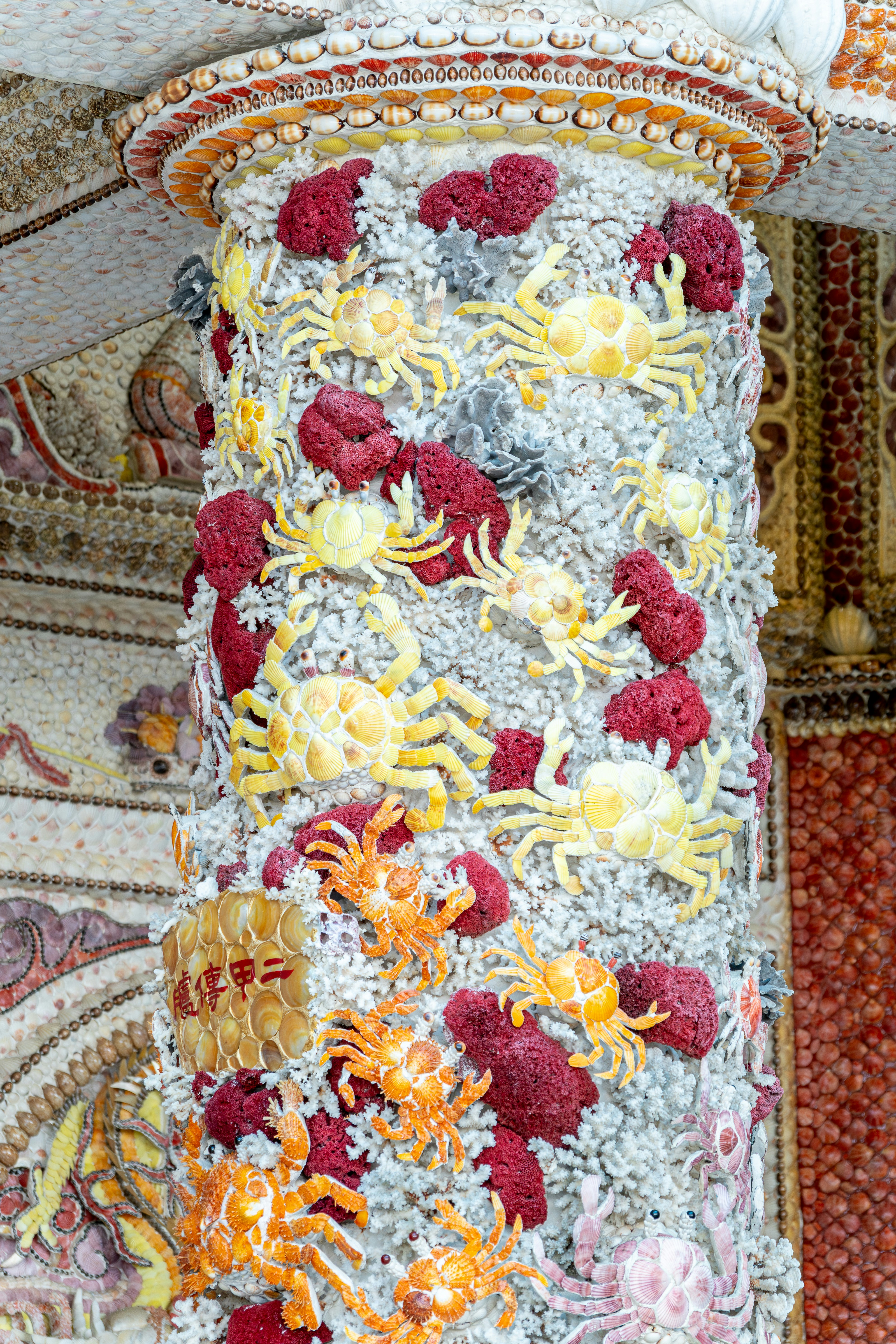 Säule, die mit zahlreichen Muscheln und Krabbenfiguren geschmückt ist.