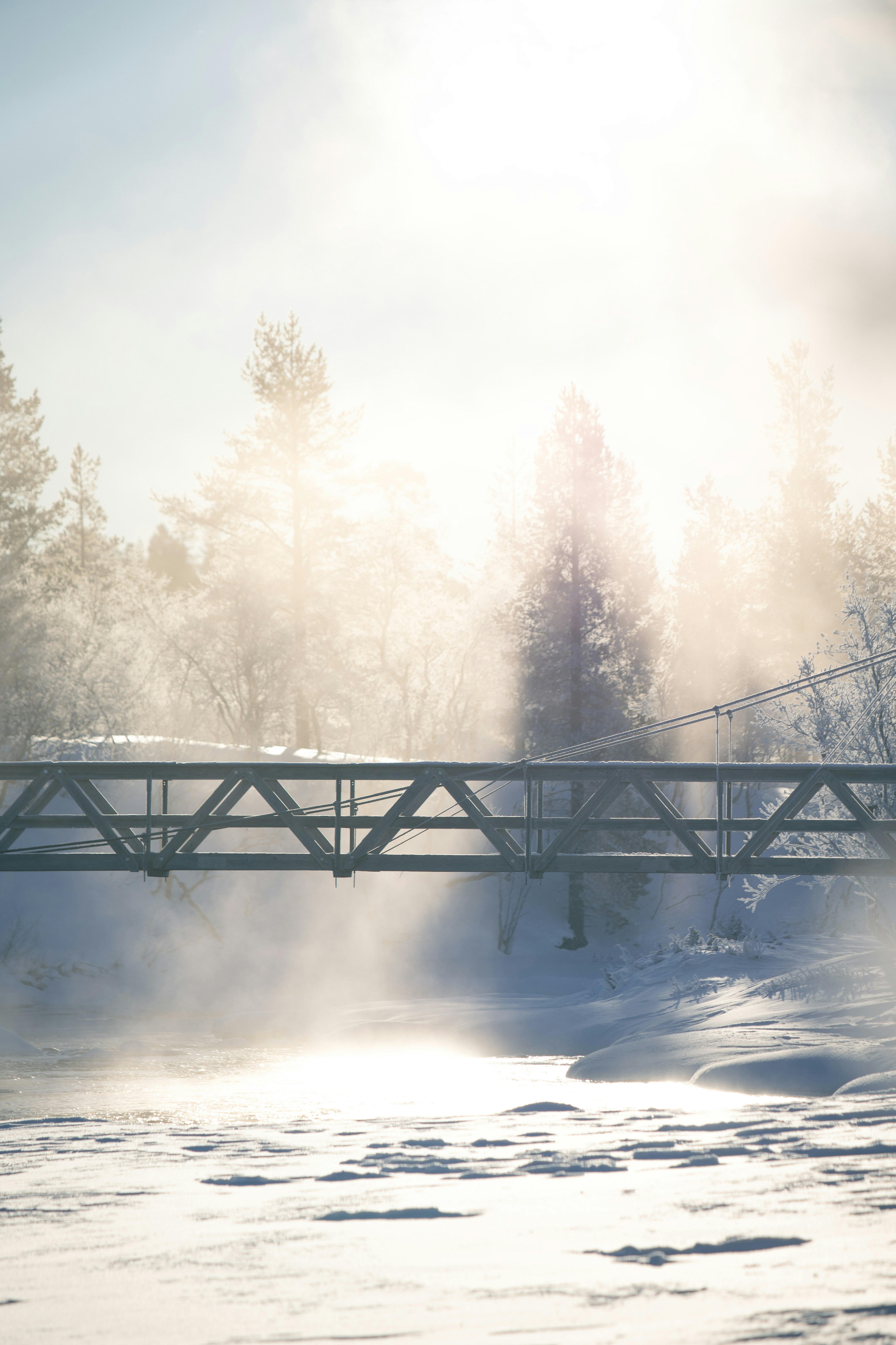 A metal bridge spans a snowy landscape with mist.