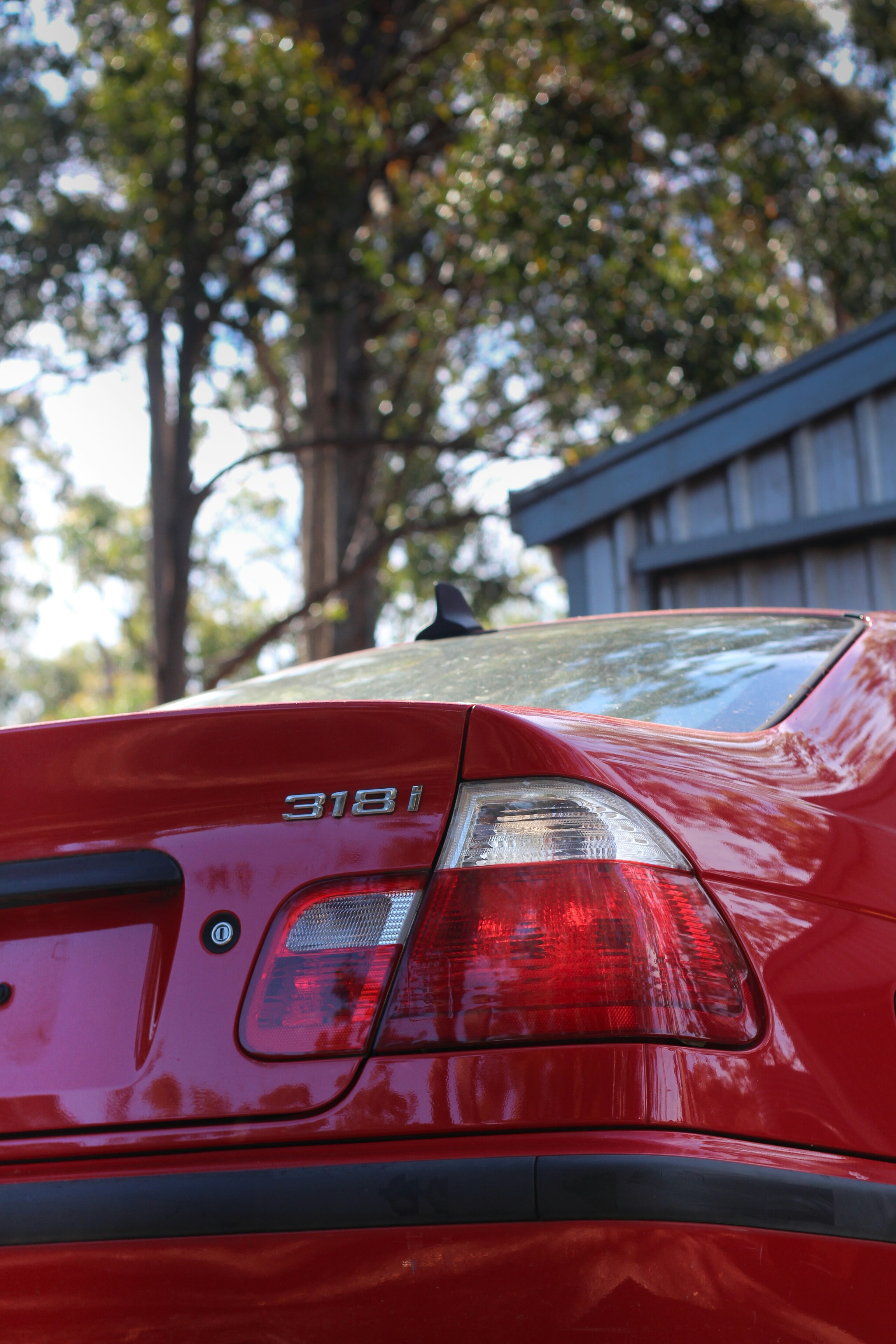 Red BMW 318i parked outdoors near trees