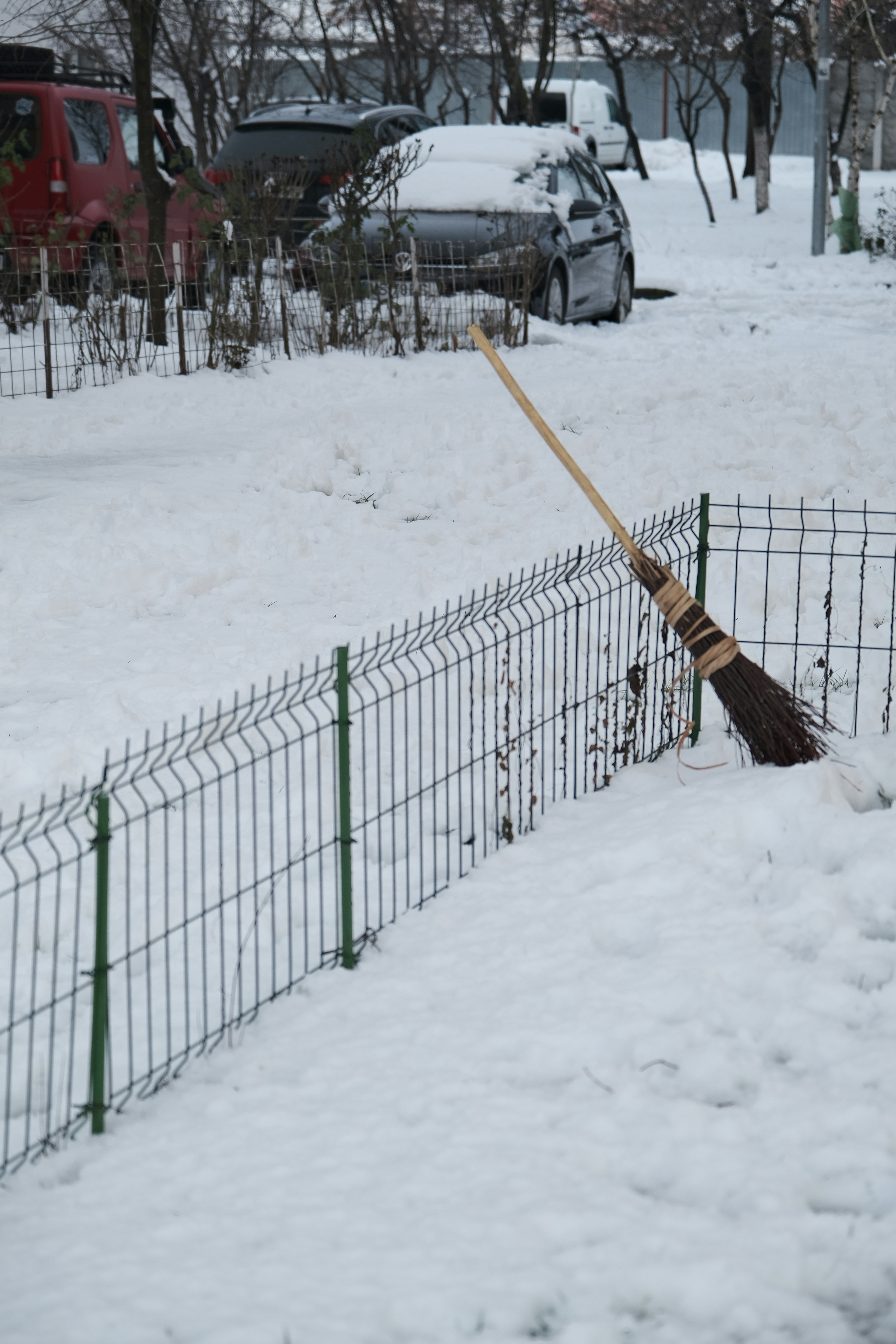 Balai appuyé contre la clôture dans la neige avec des voitures couvertes de neige