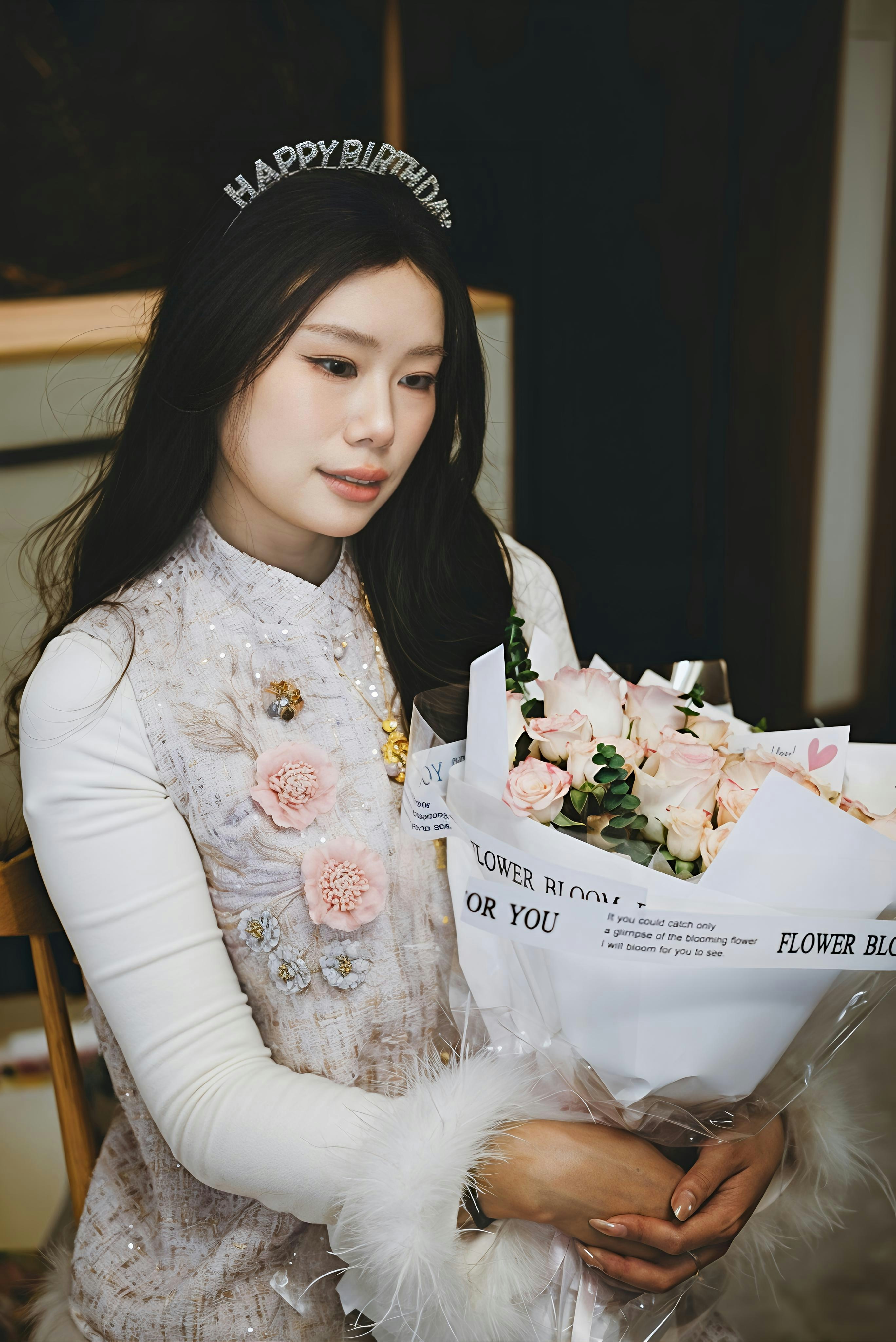 Woman wearing a happy birthday headband holding flowers