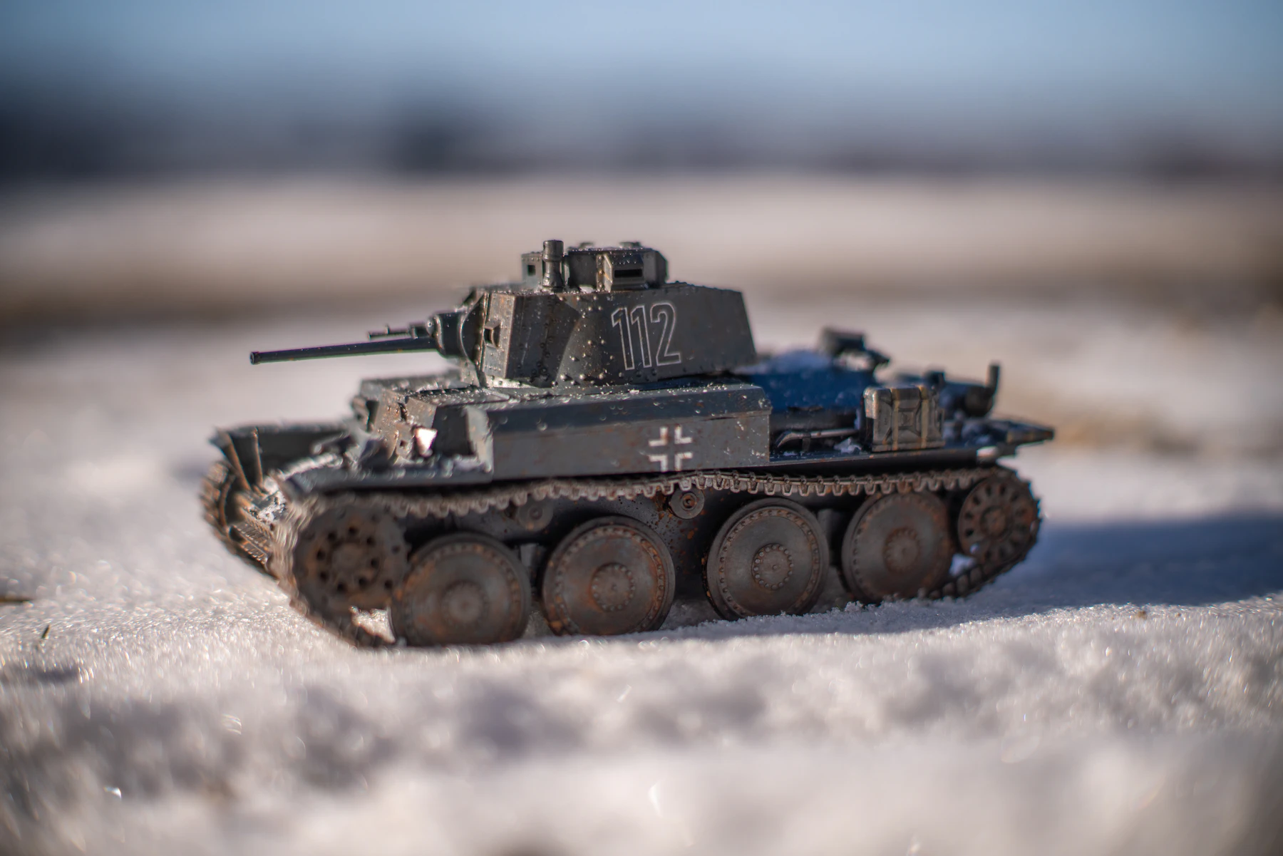 A dark gray model tank numbered 112 on snow, with rust and dirt worked into its tracks