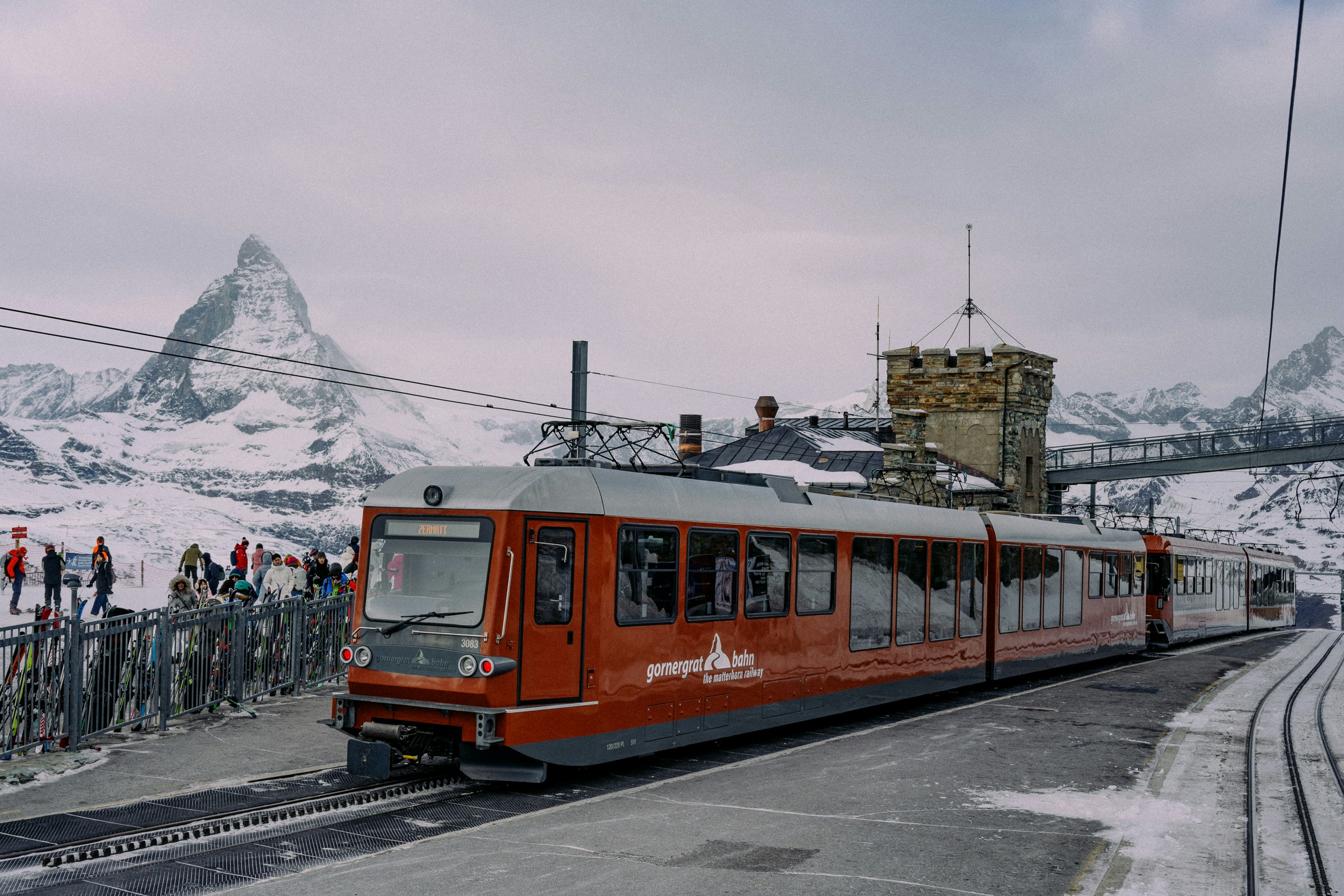 Red train on snowy tracks with matterhorn mountain.