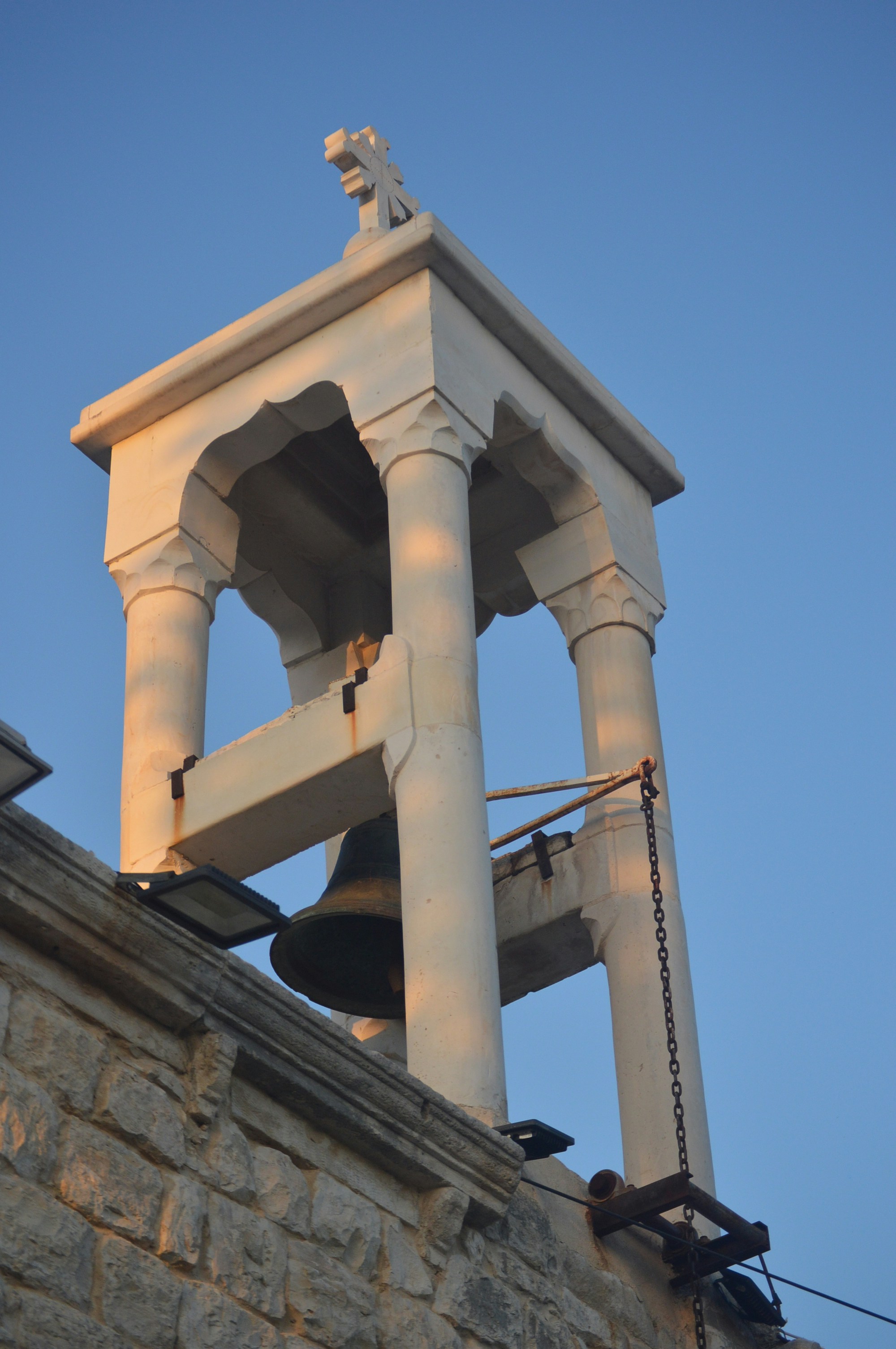Stone bell tower with a large bell against blue sky