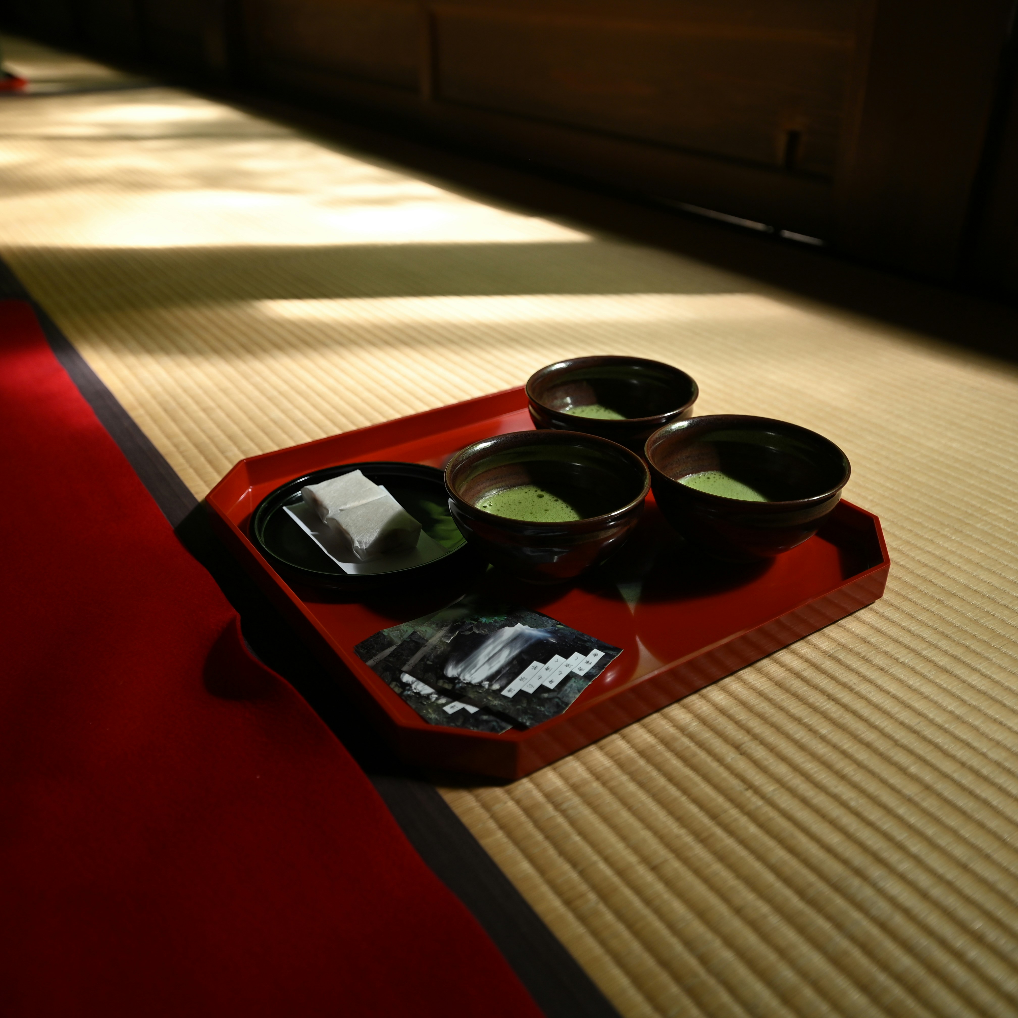 Tray with tea bowls and sweets on tatami mat.