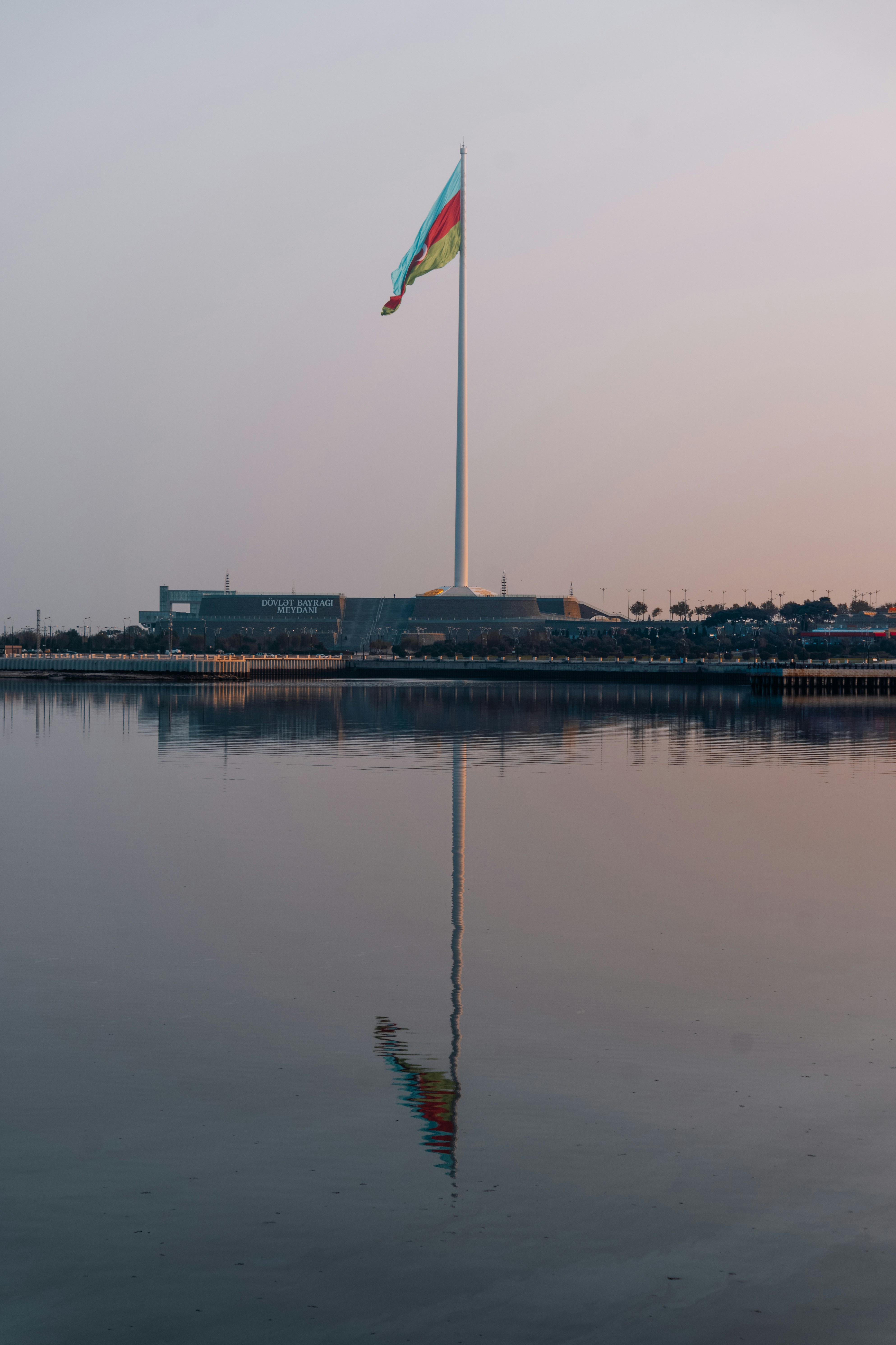 Tall flagpole with flag reflected in calm water