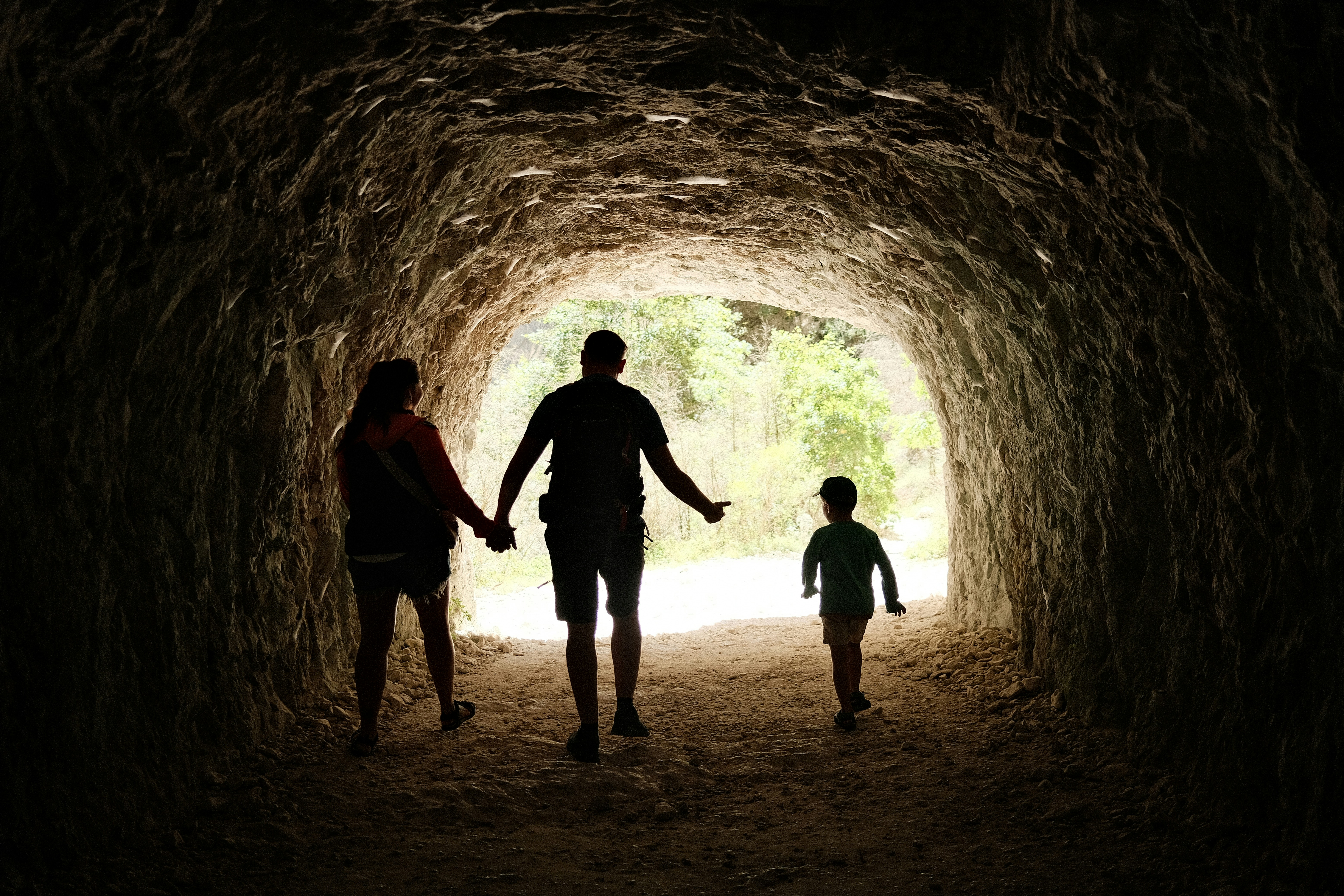 Family walking through a dark cave tunnel towards light.