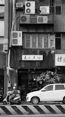 Motorcyclist and car parked by building with air conditioners.