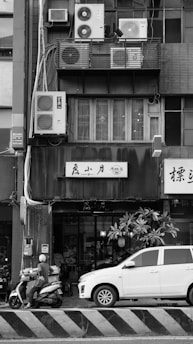 Motorcyclist and car parked by building with air conditioners.