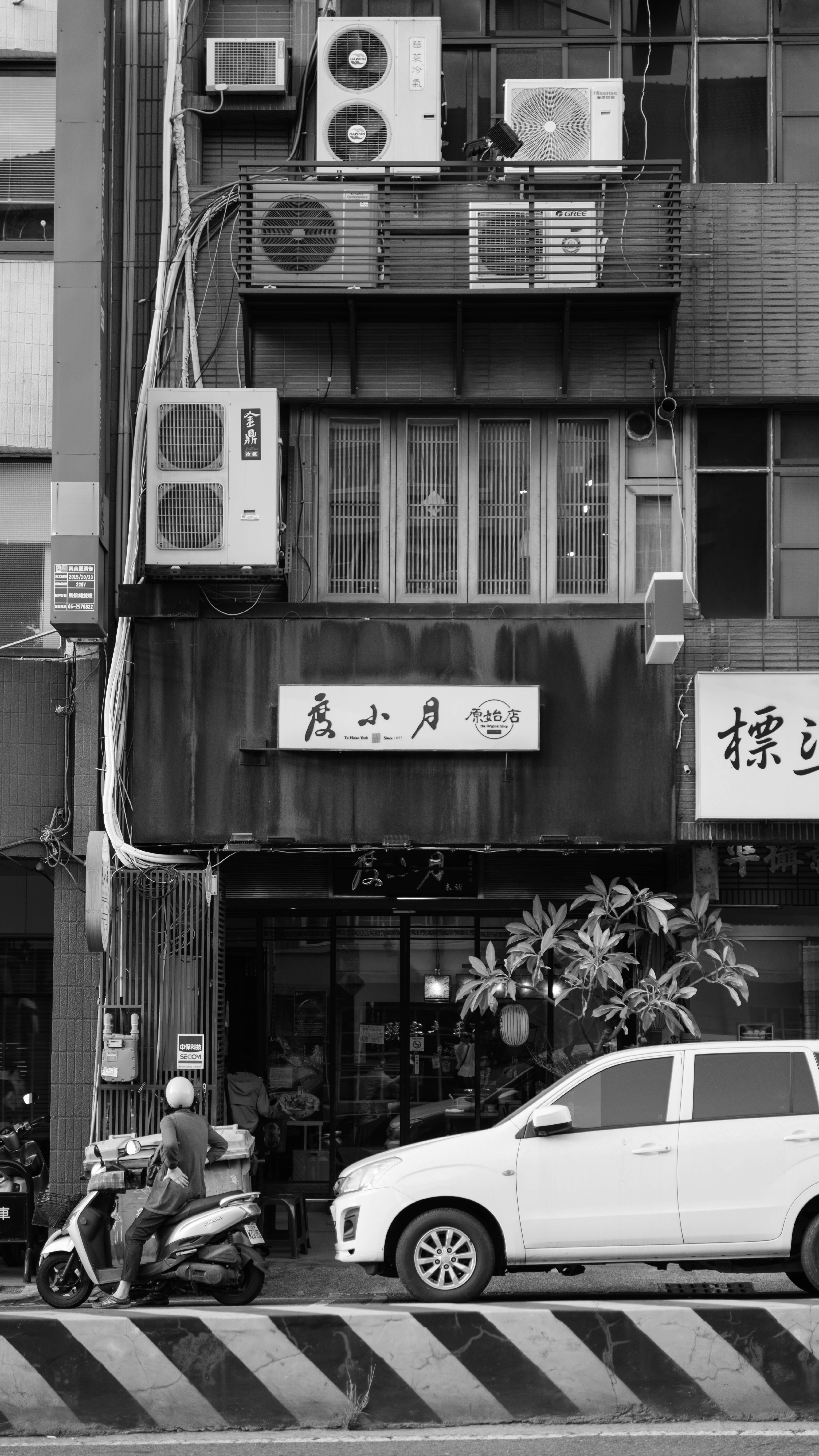 Motorcyclist and car parked by building with air conditioners.