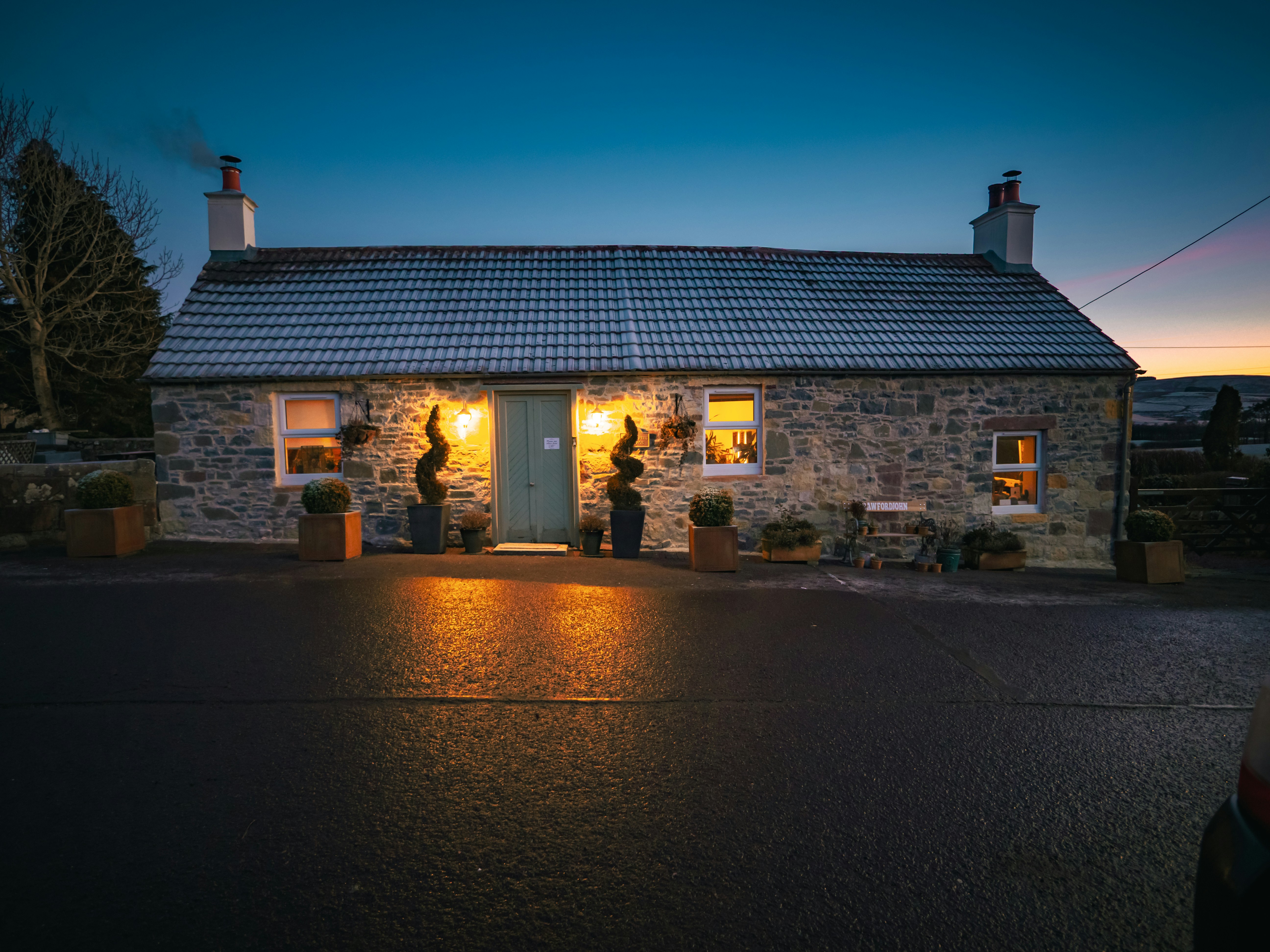 Stone cottage illuminated at dusk with warm lights.