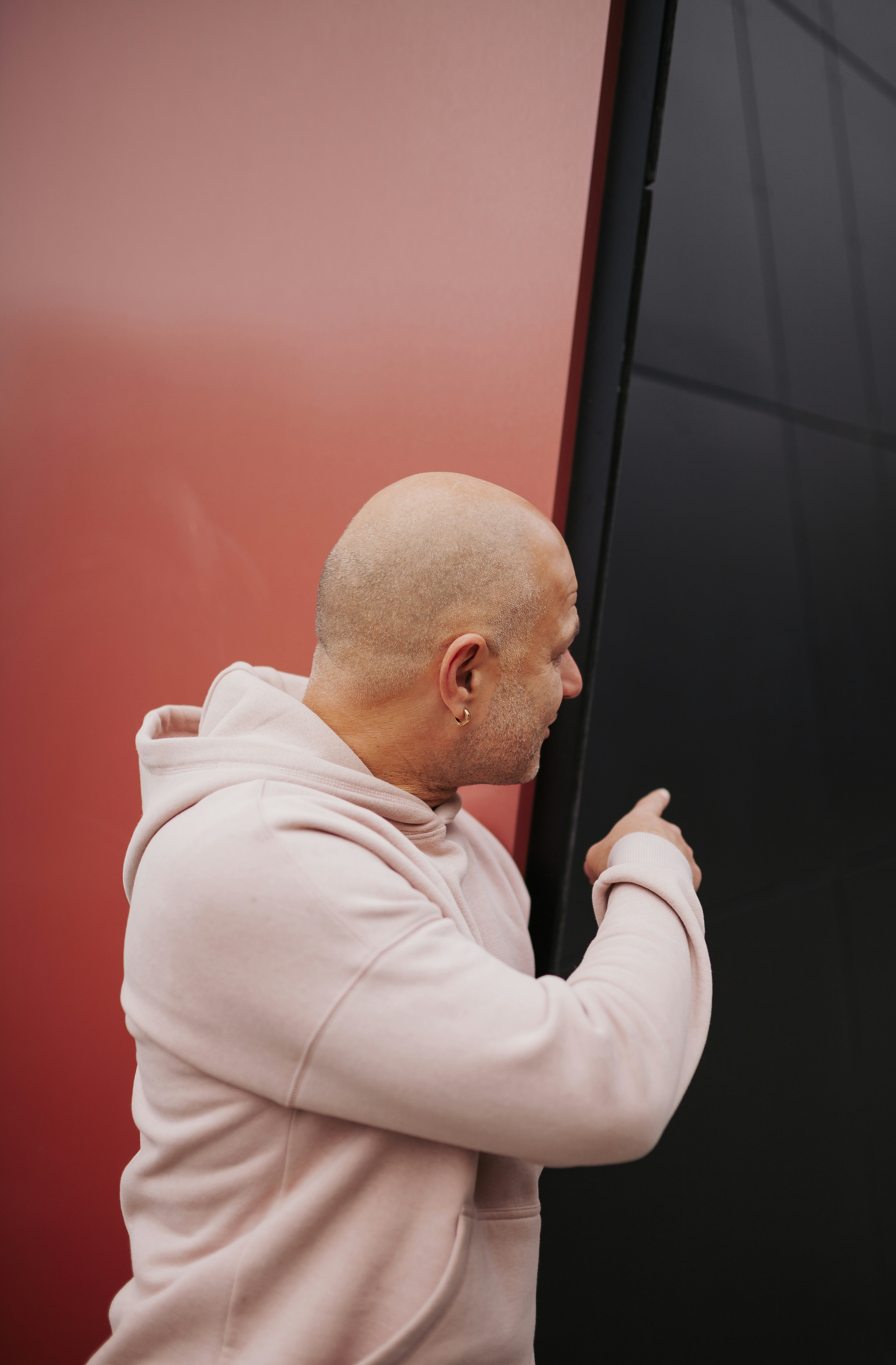 Bald man in pink hoodie touches dark wall