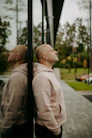 Bald man in hoodie leans against glass building