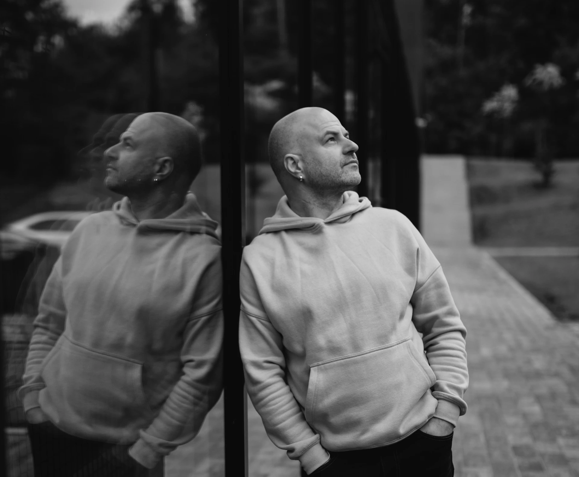 Bald man in hoodie leans against reflective surface