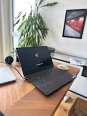 Open black laptop on a wooden desk with plant.