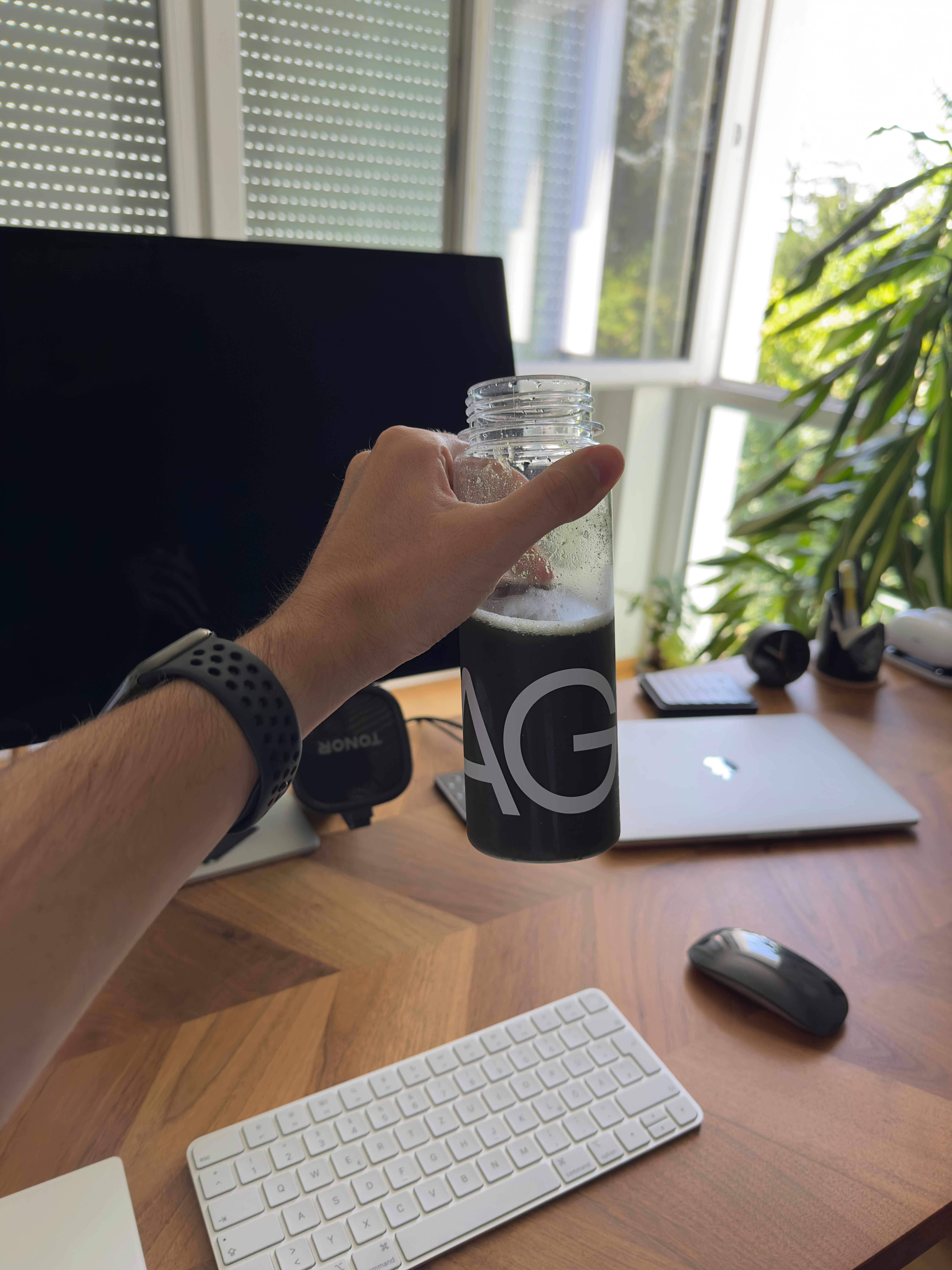 Hand holding a bottle of green liquid at desk.