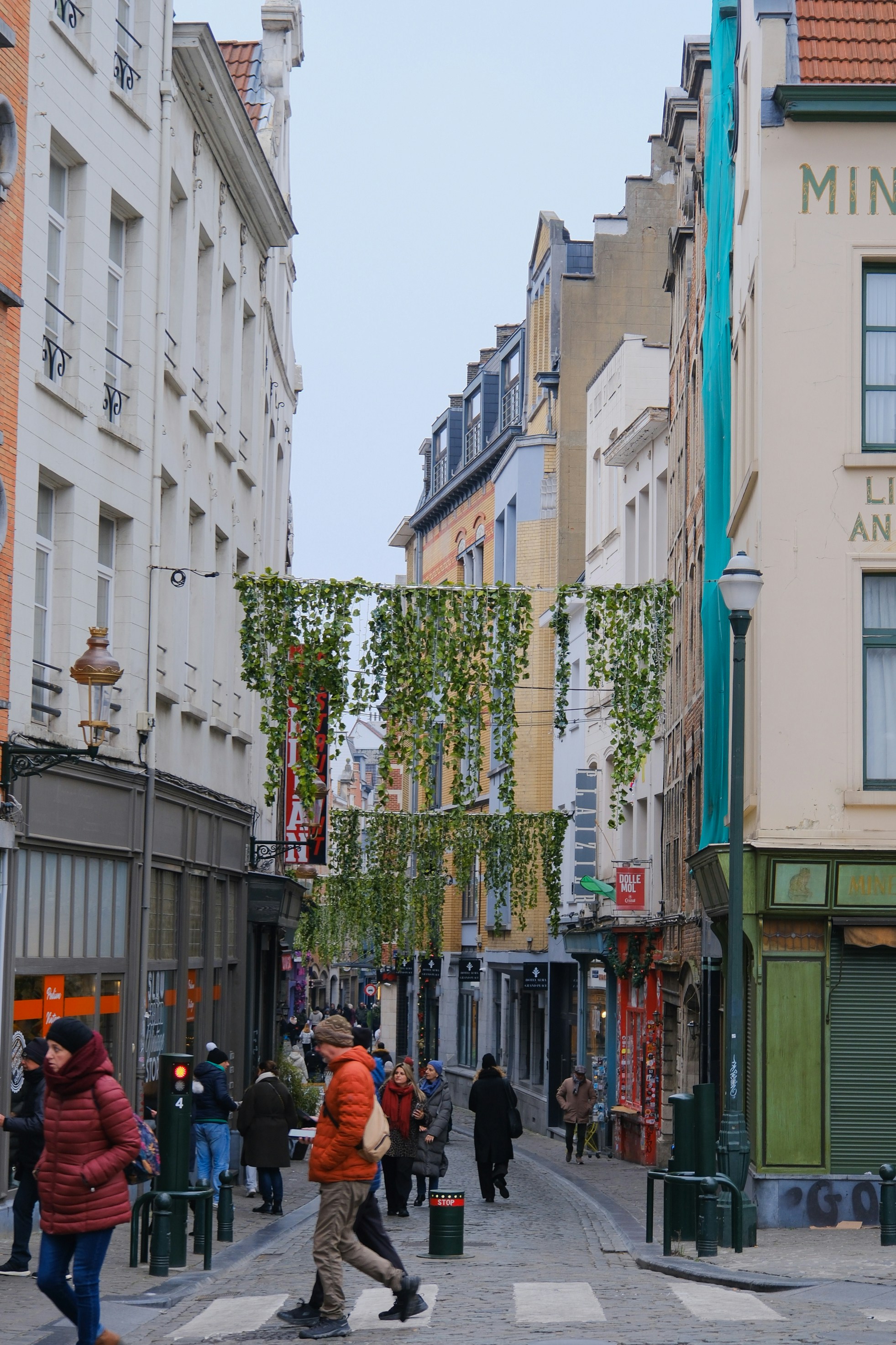 People walking down a narrow street decorated with greenery.