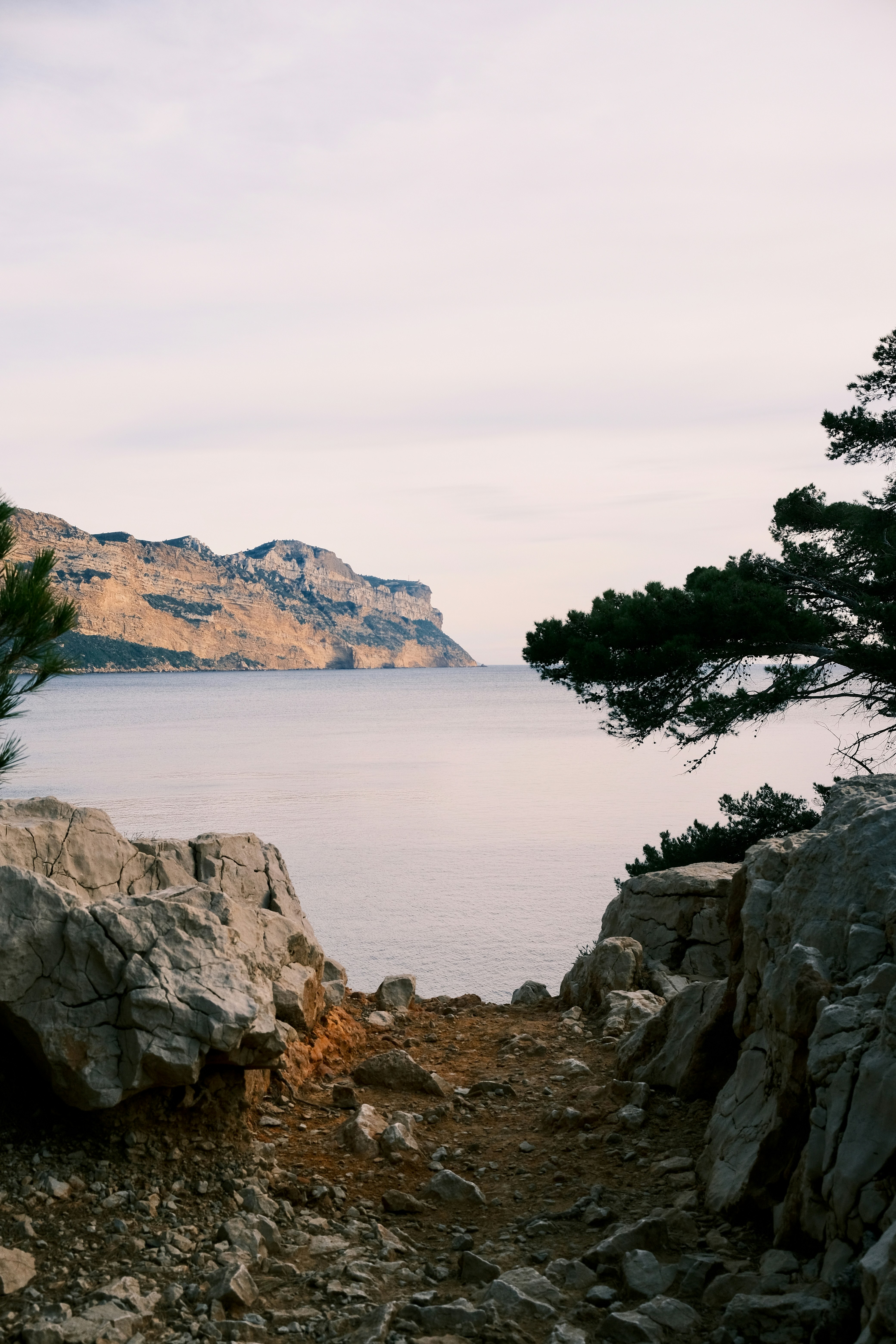 Sentiero roccioso che conduce a un mare calmo e a scogliere lontane.