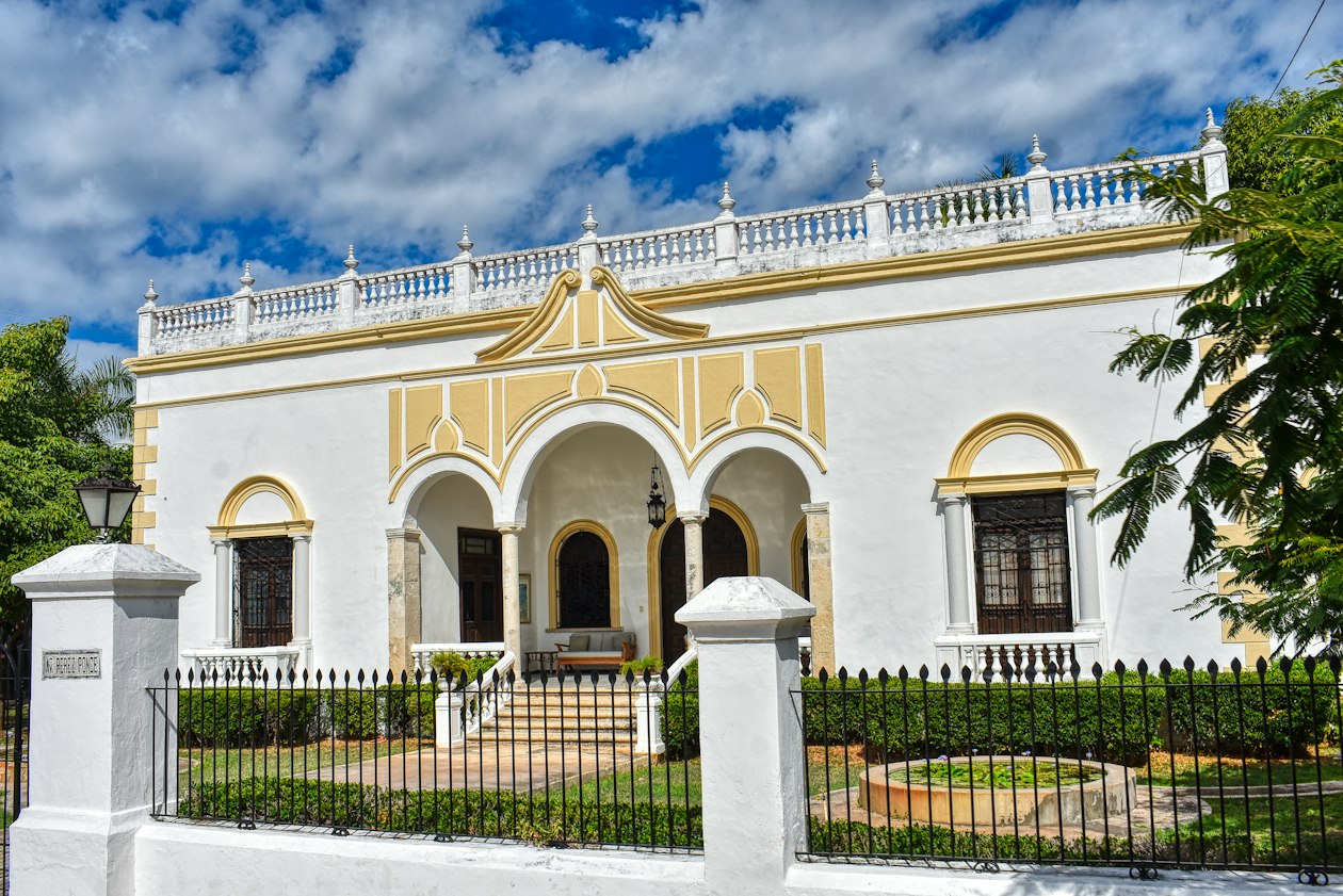White and yellow early 20th-century mansion with arched porch and balustrade in Merida, one of the city's draws in the Merida vs Valladolid choice
