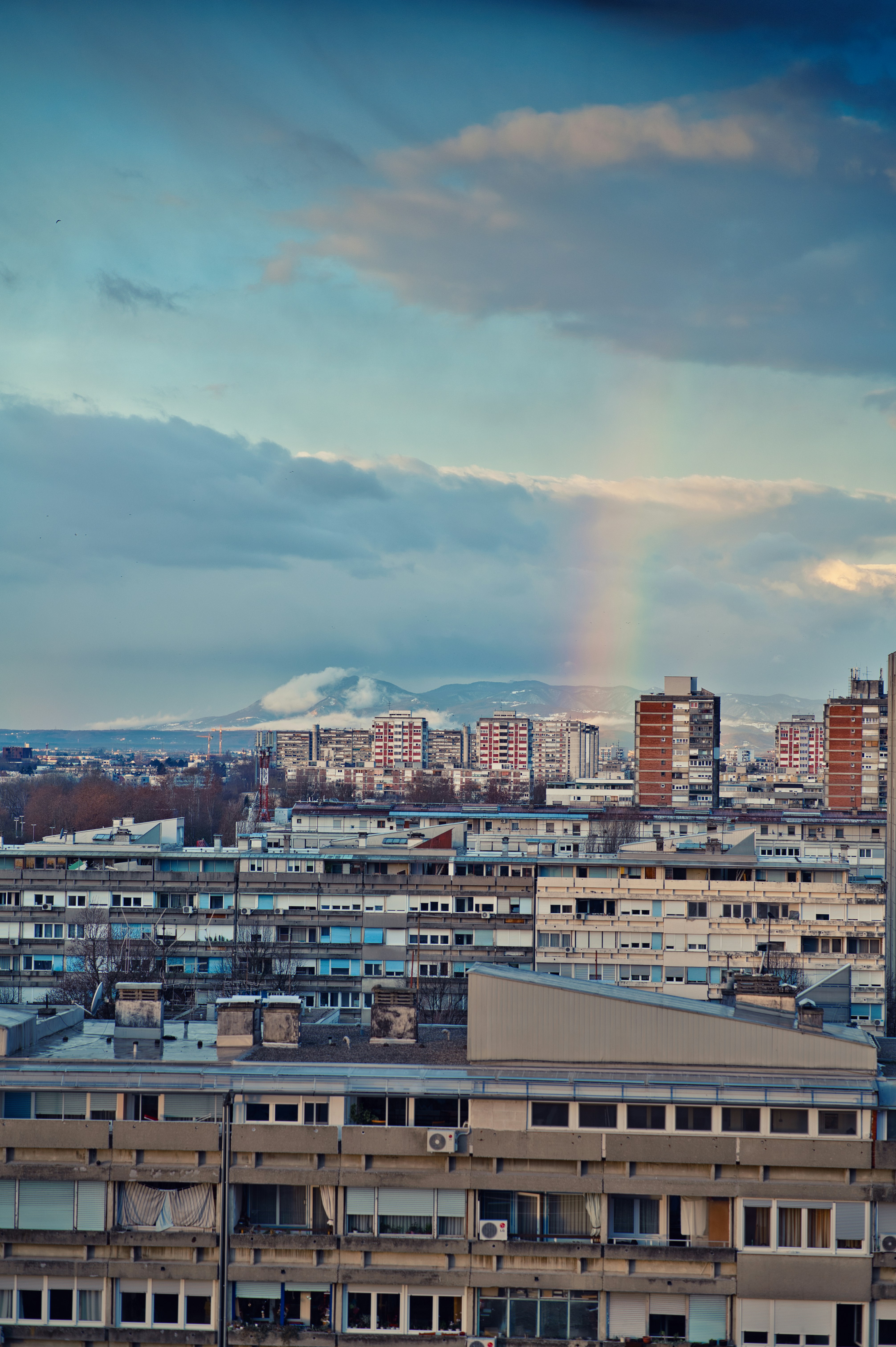 Apartment buildings under a rainbow and snowy mountains.