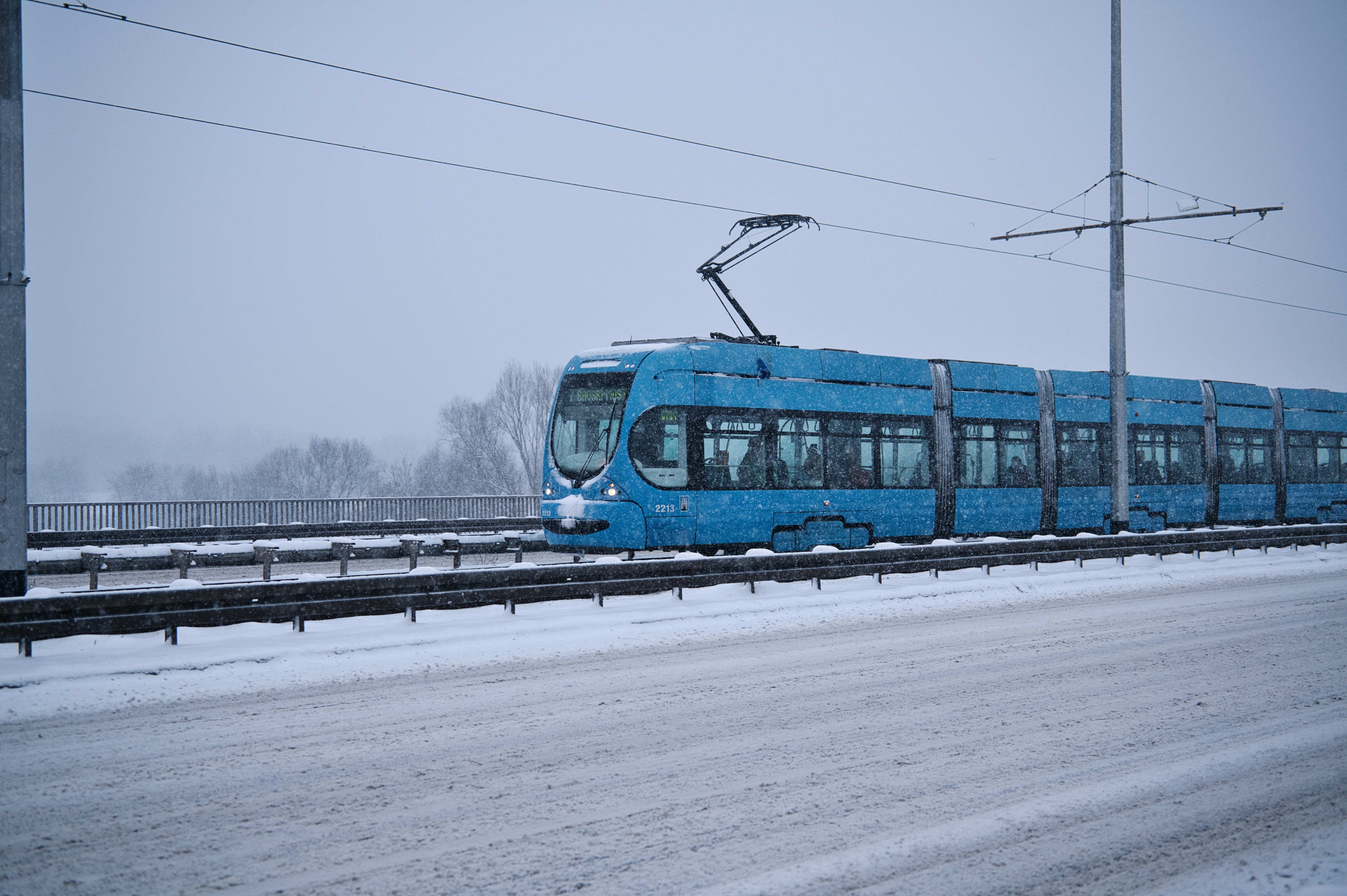 A blue tram travels on tracks during a snowstorm.