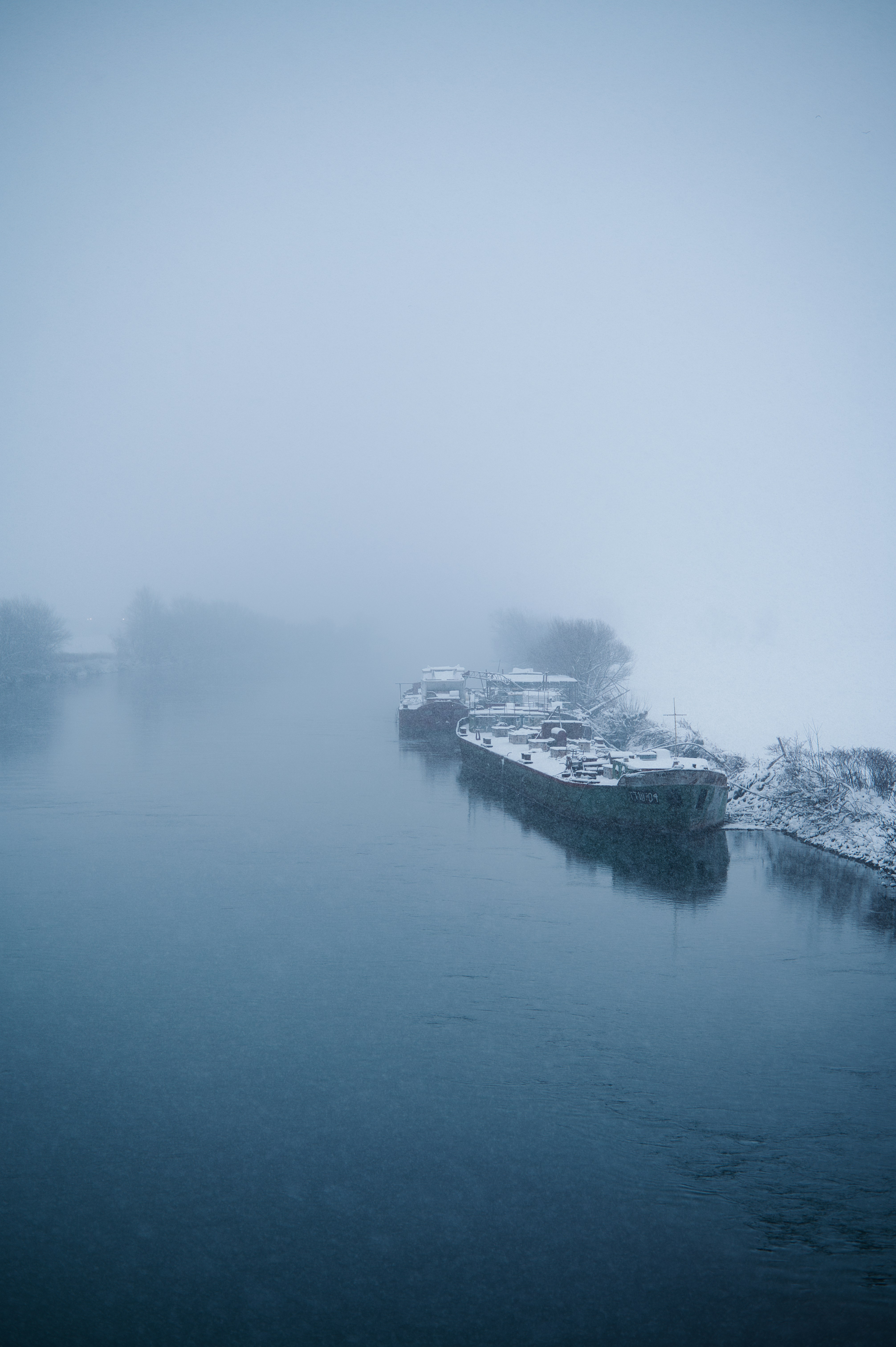 Two barges docked on a foggy winter river.