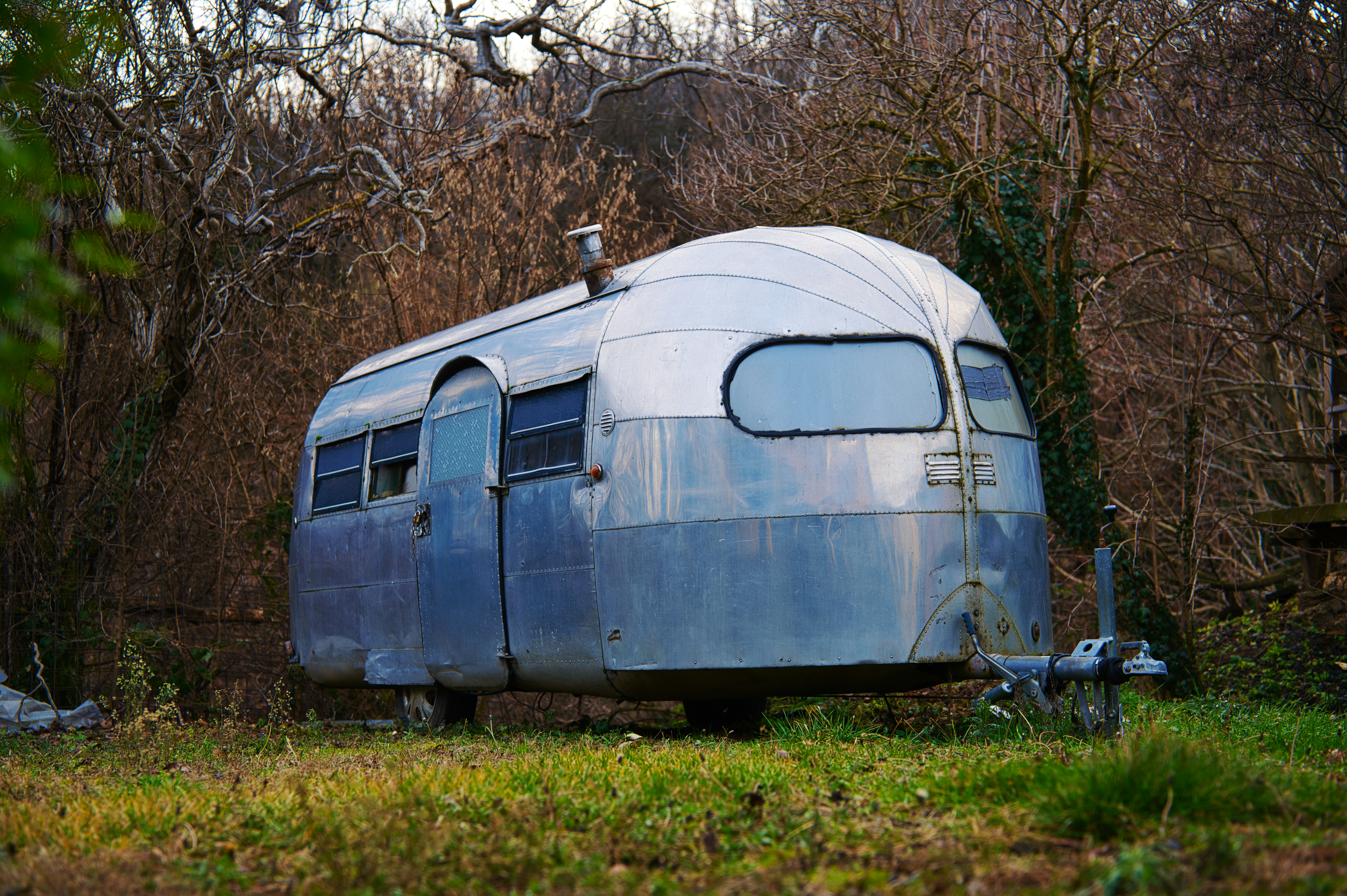Vintage silver travel trailer parked in grassy field.