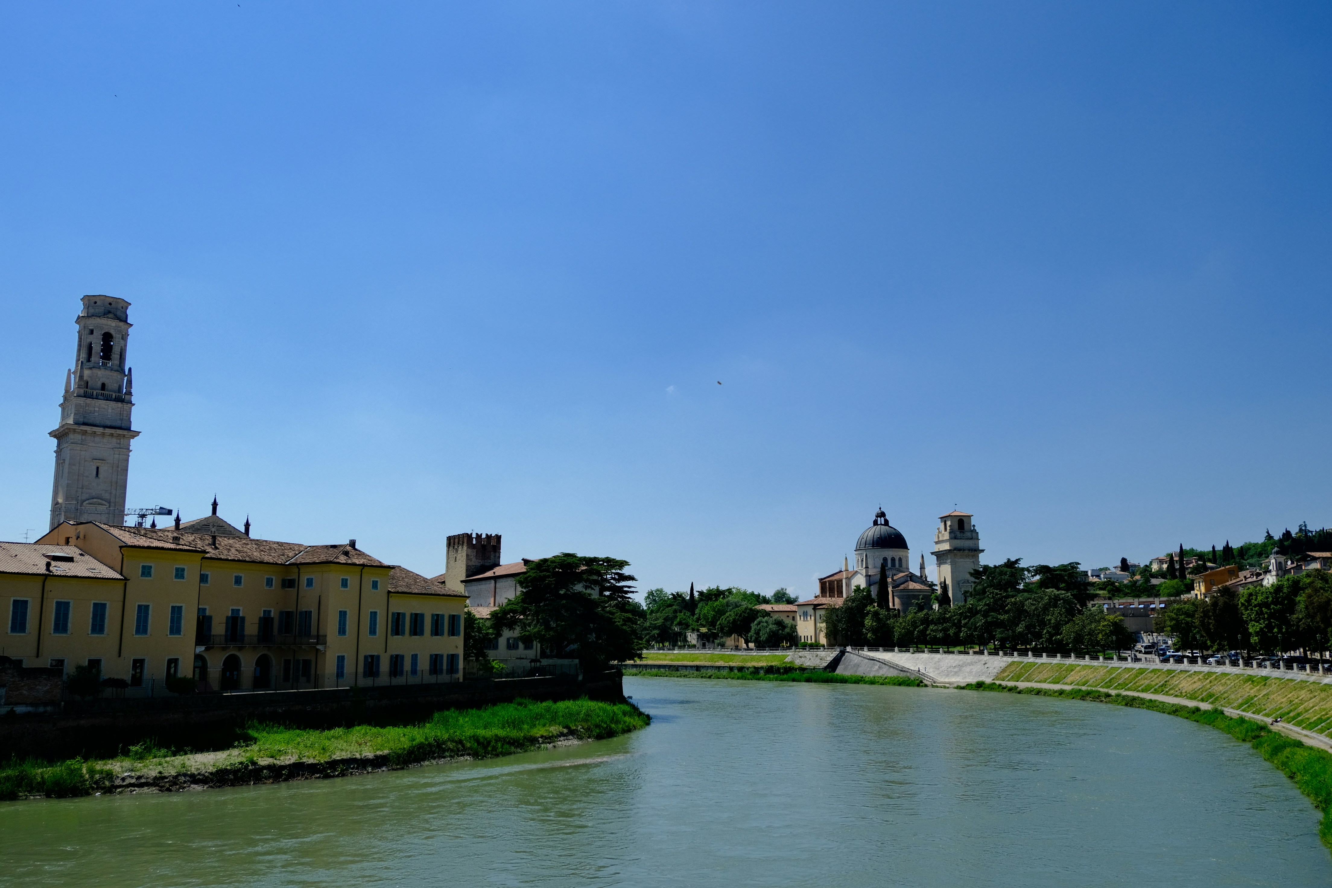 River flows past buildings under a clear blue sky.