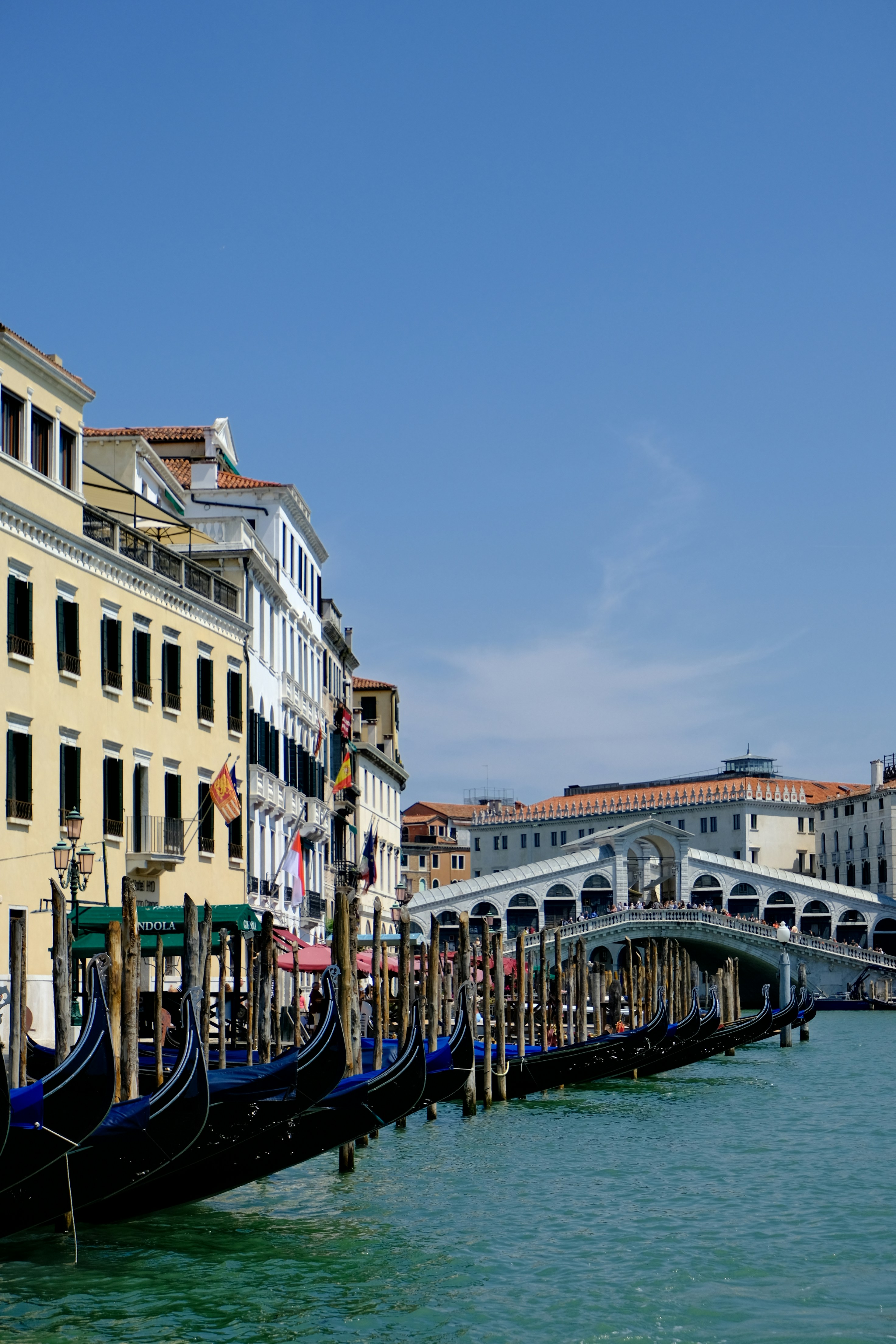 Gondolas docked along a canal with rialto bridge.