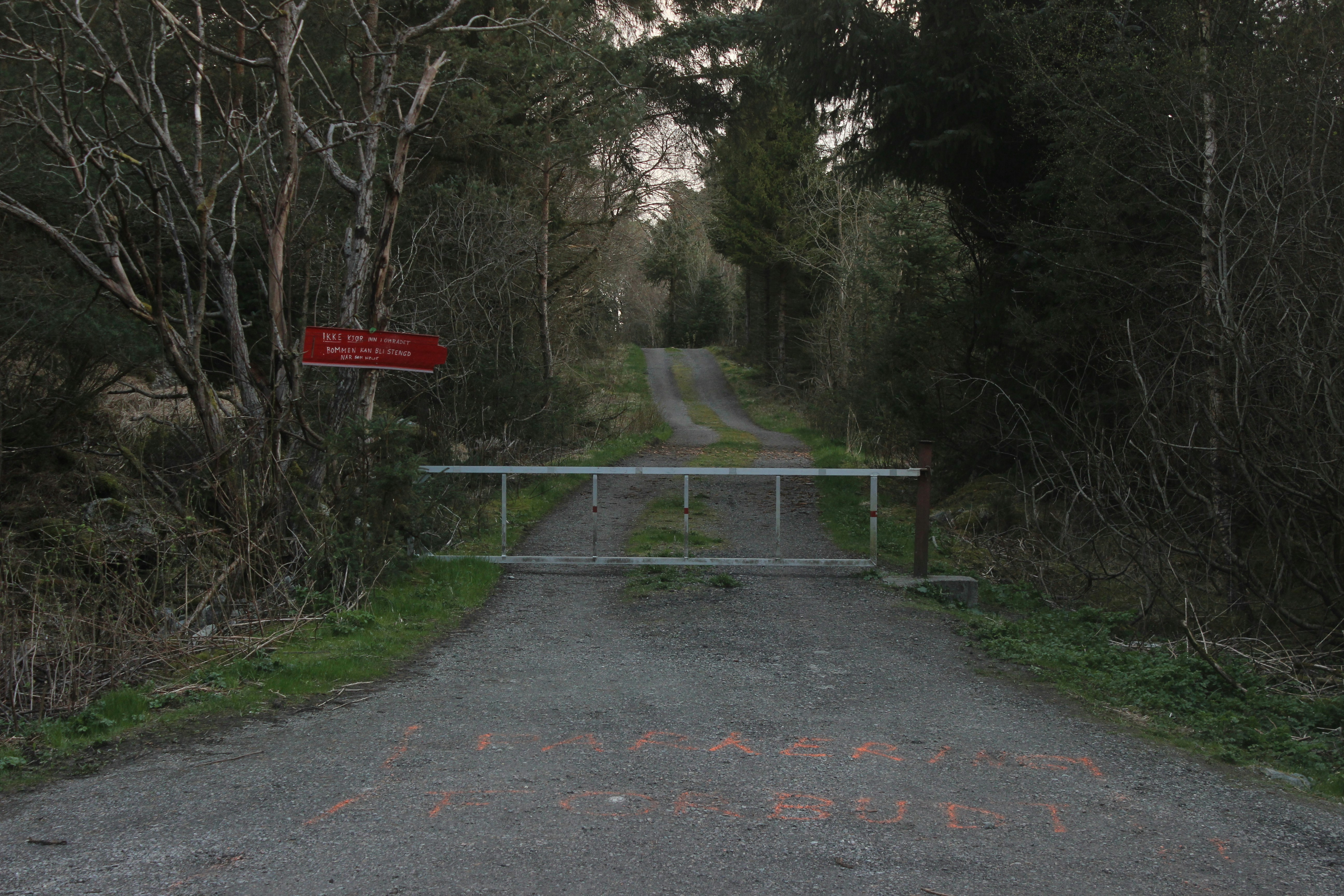 Gravel road blocked by metal bar and sign