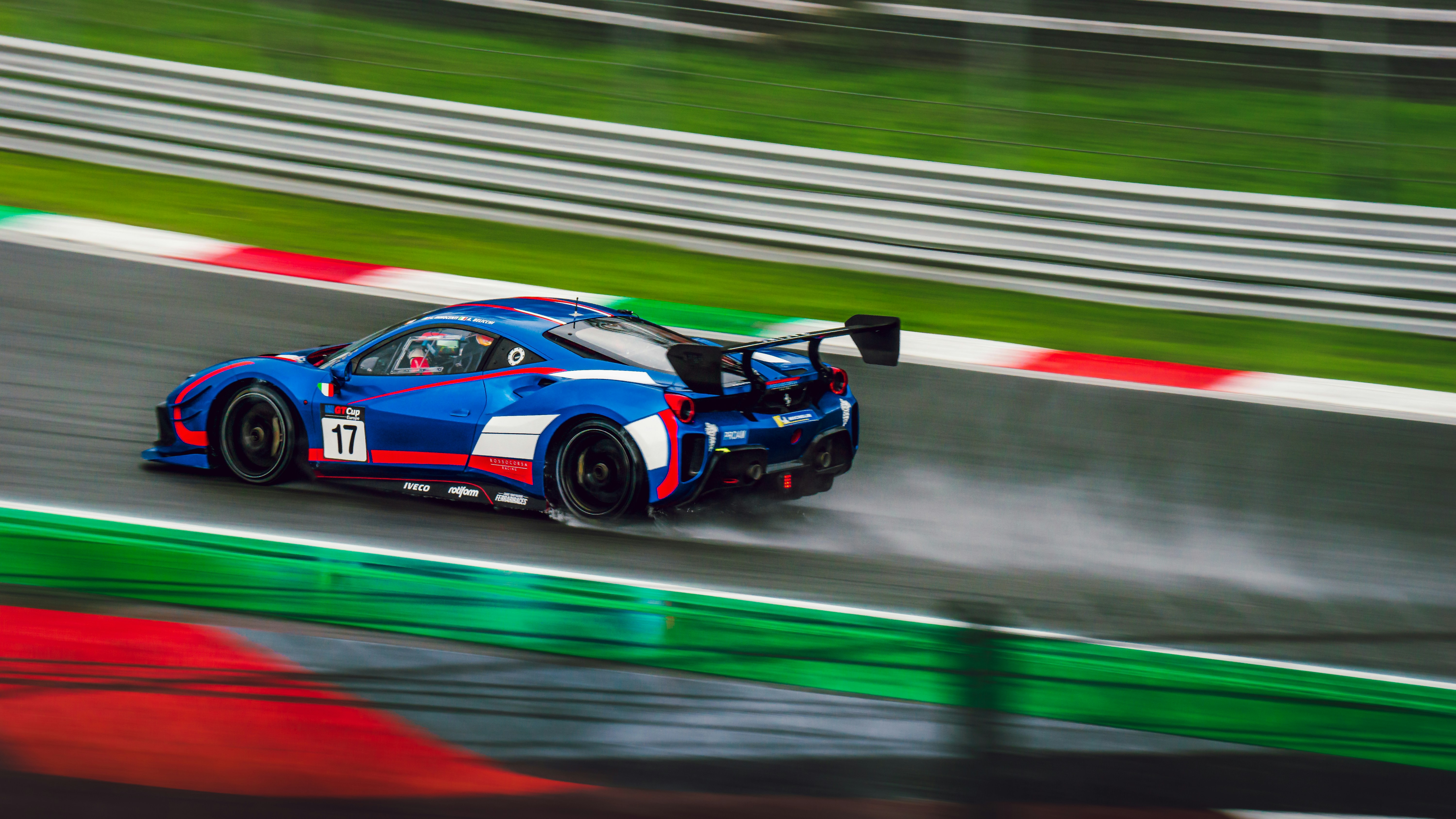 A blue race car speeds around a wet track.