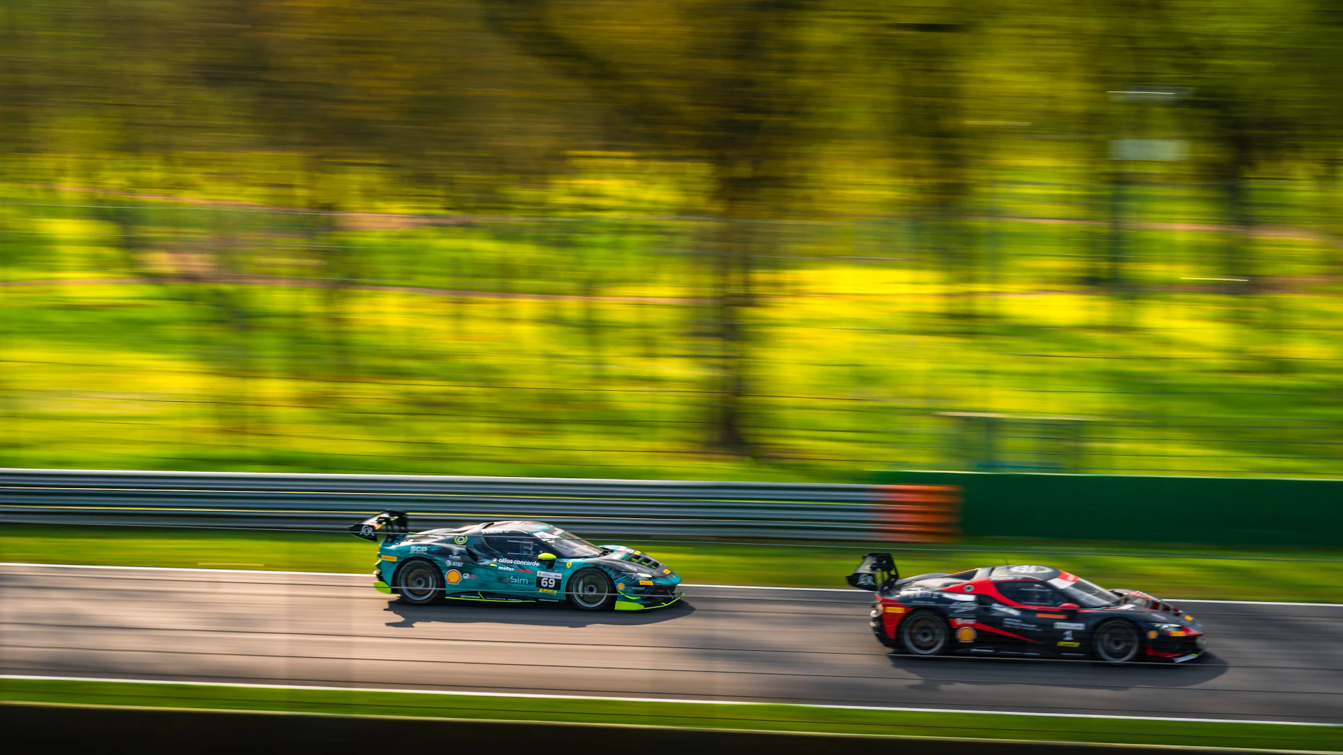 Two race cars speed down a track with trees blurred.