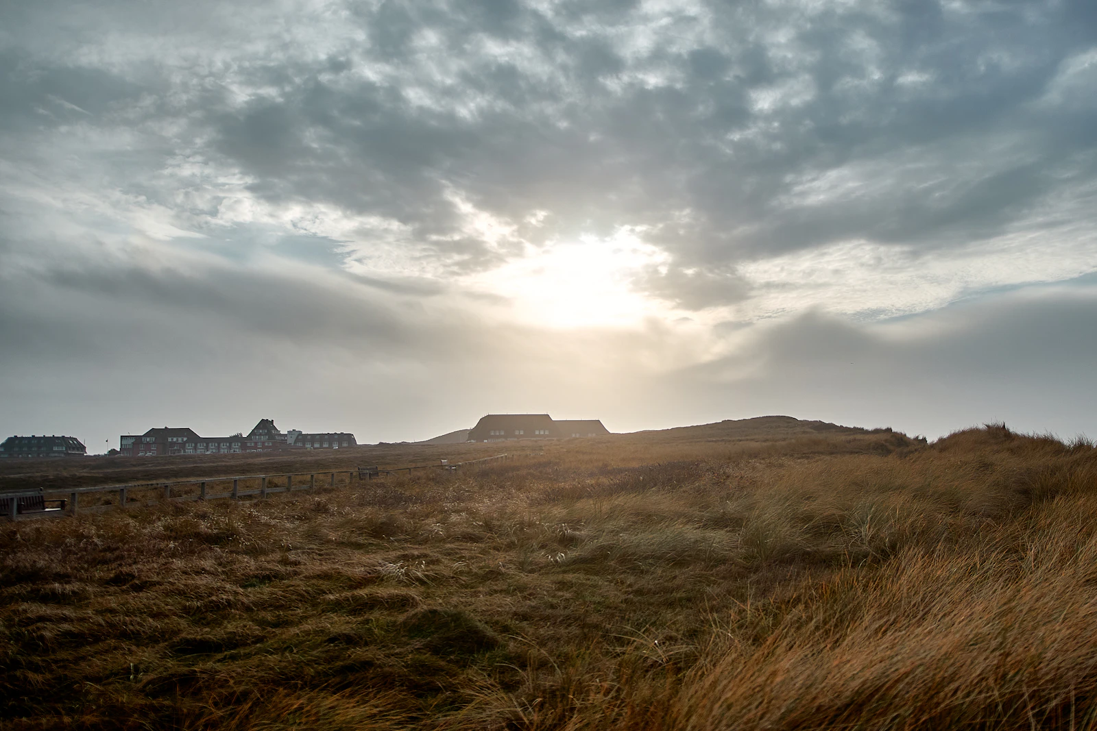 Sunlight breaks through cloudy sky over grassy dunes