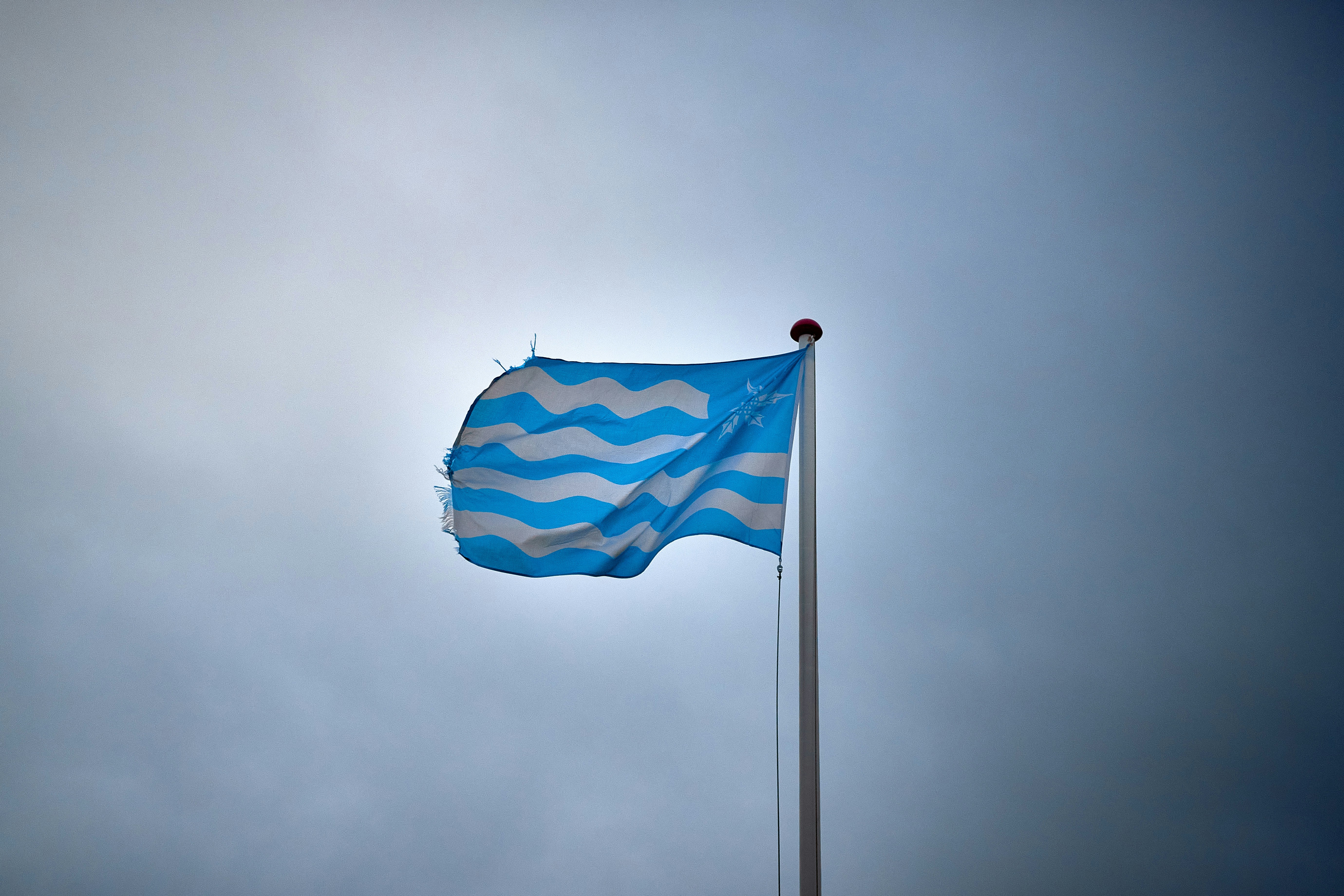 A blue flag with white wavy stripes on a flagpole.