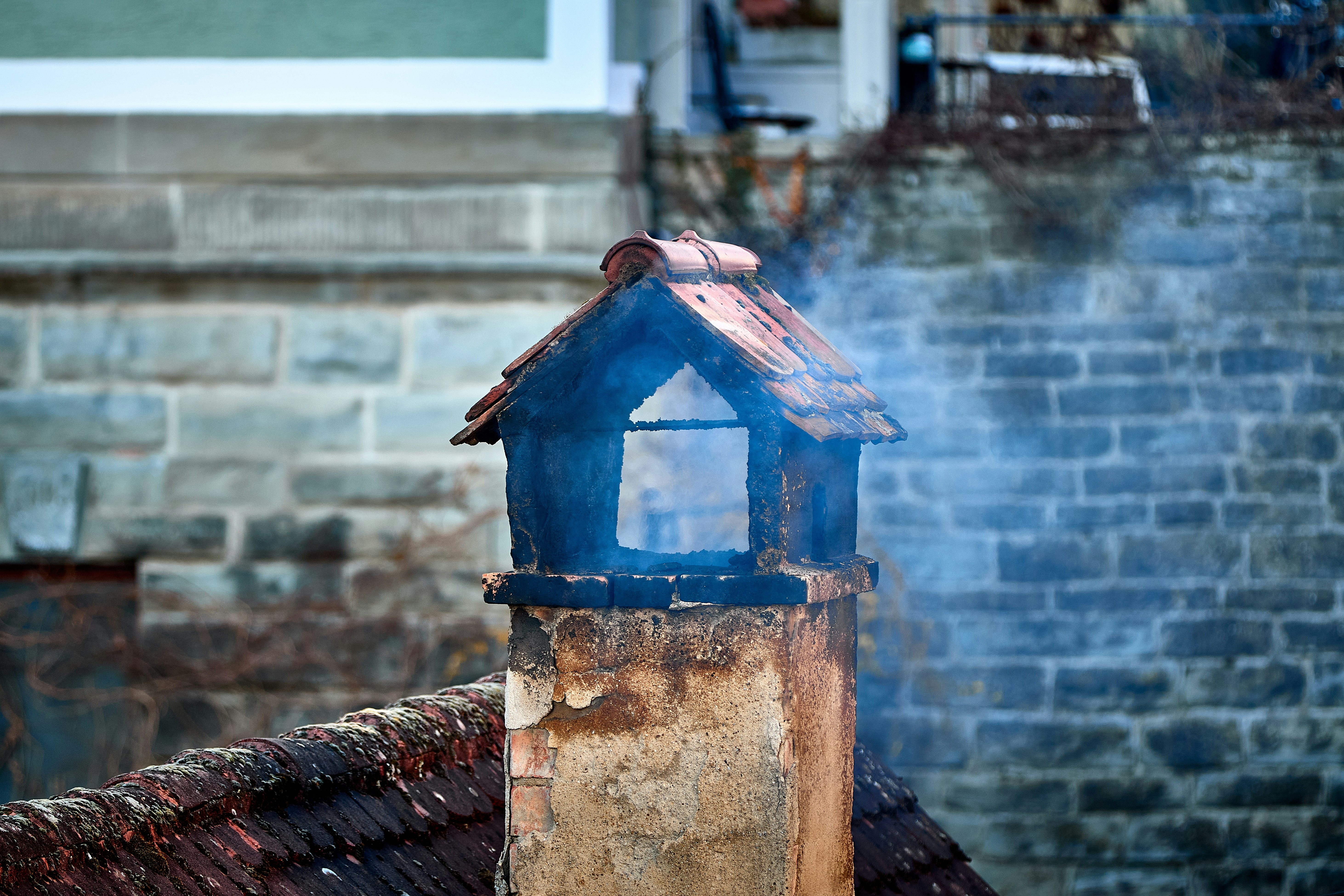 Smoke rising from a rustic chimney on a brick building.
