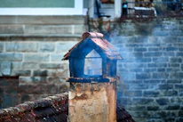 Smoke rising from a rustic chimney on a brick building.