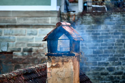 Smoke rising from a rustic chimney on a brick building.