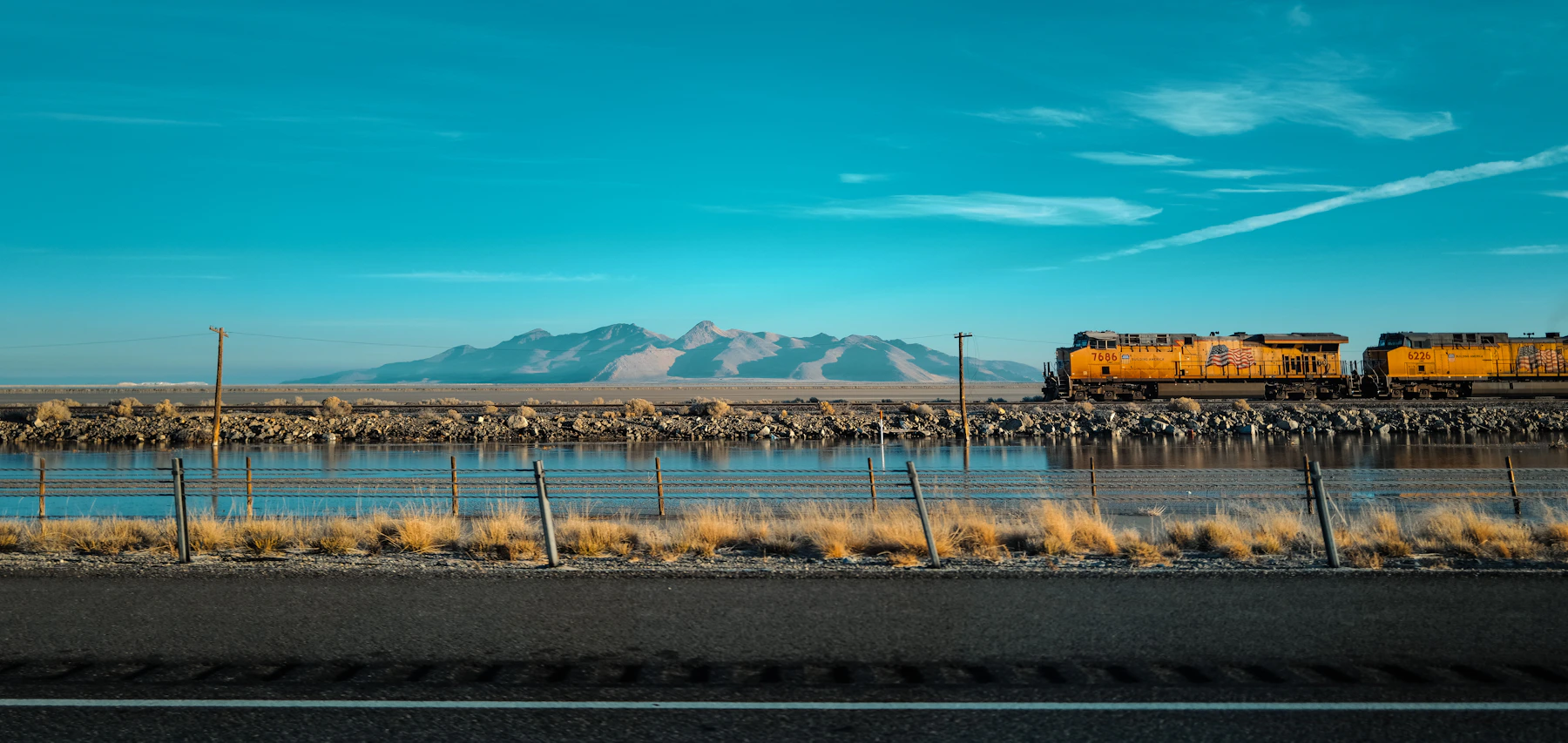A Union Pacific freight train running along a lakeshore with mountains behind it