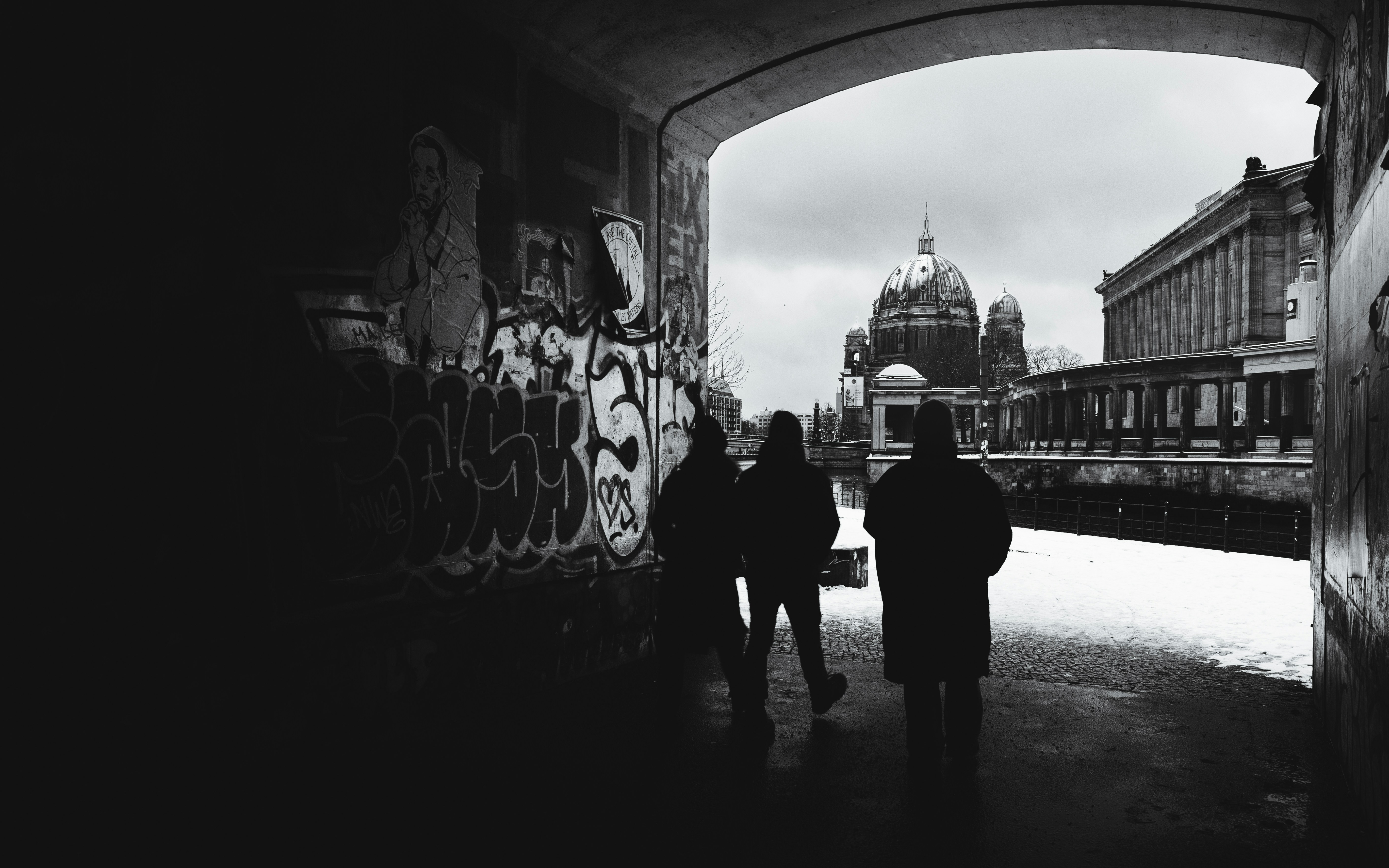 Three figures walk through a dark tunnel towards a dome.
