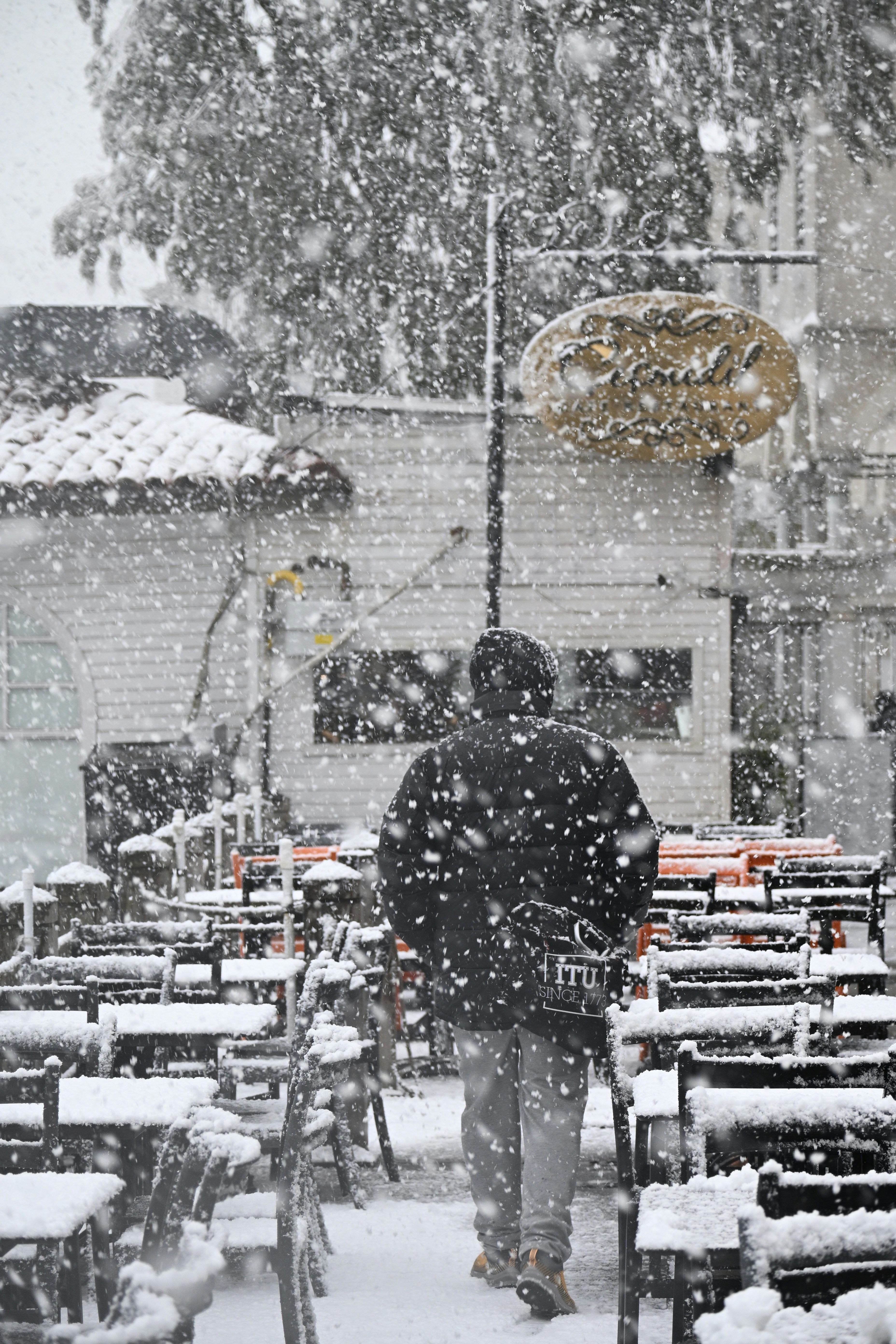 A person walks through a snowy outdoor cafe.
