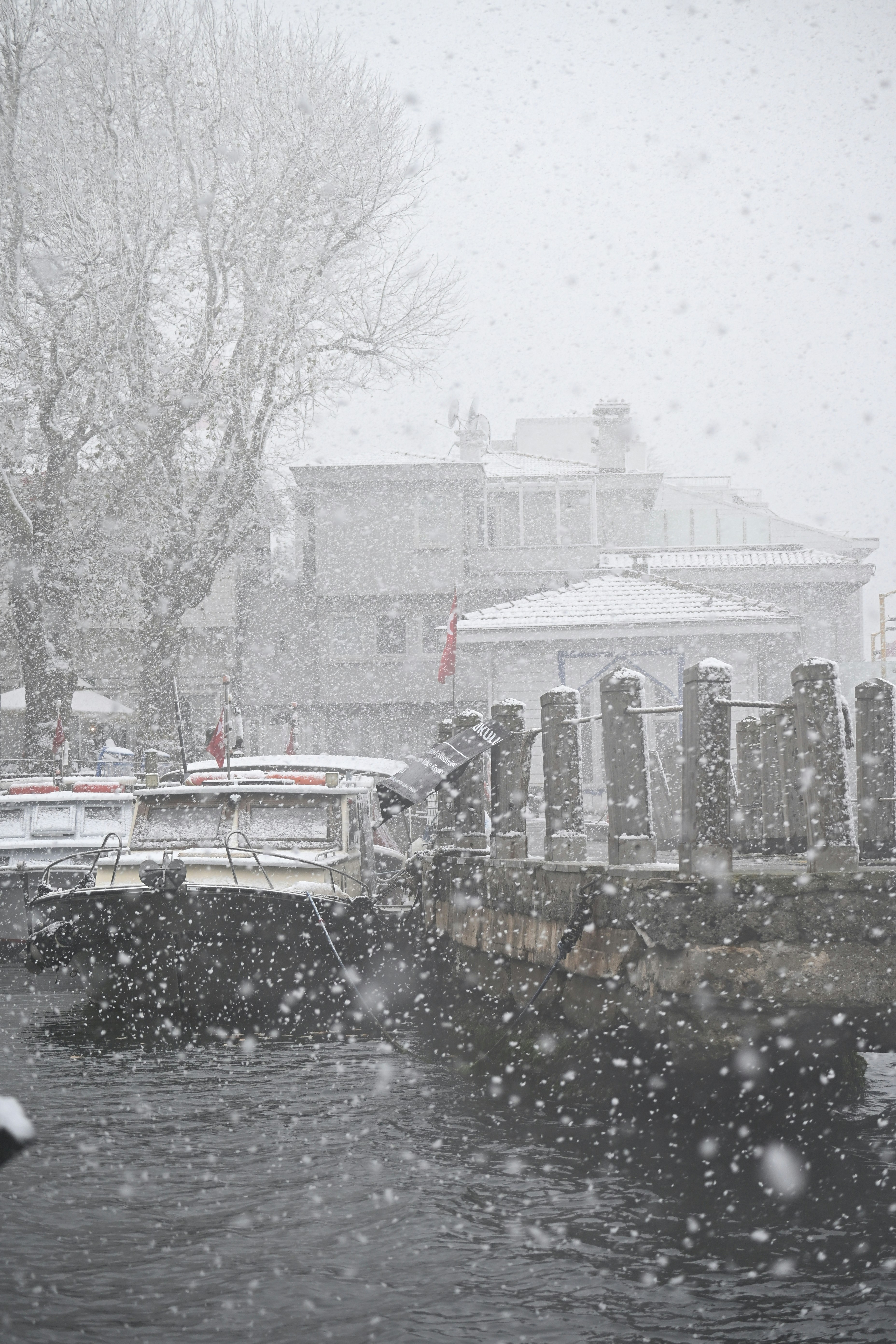 Boats docked at a pier during a heavy snowfall.