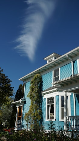 A blue victorian house under a wispy cloud