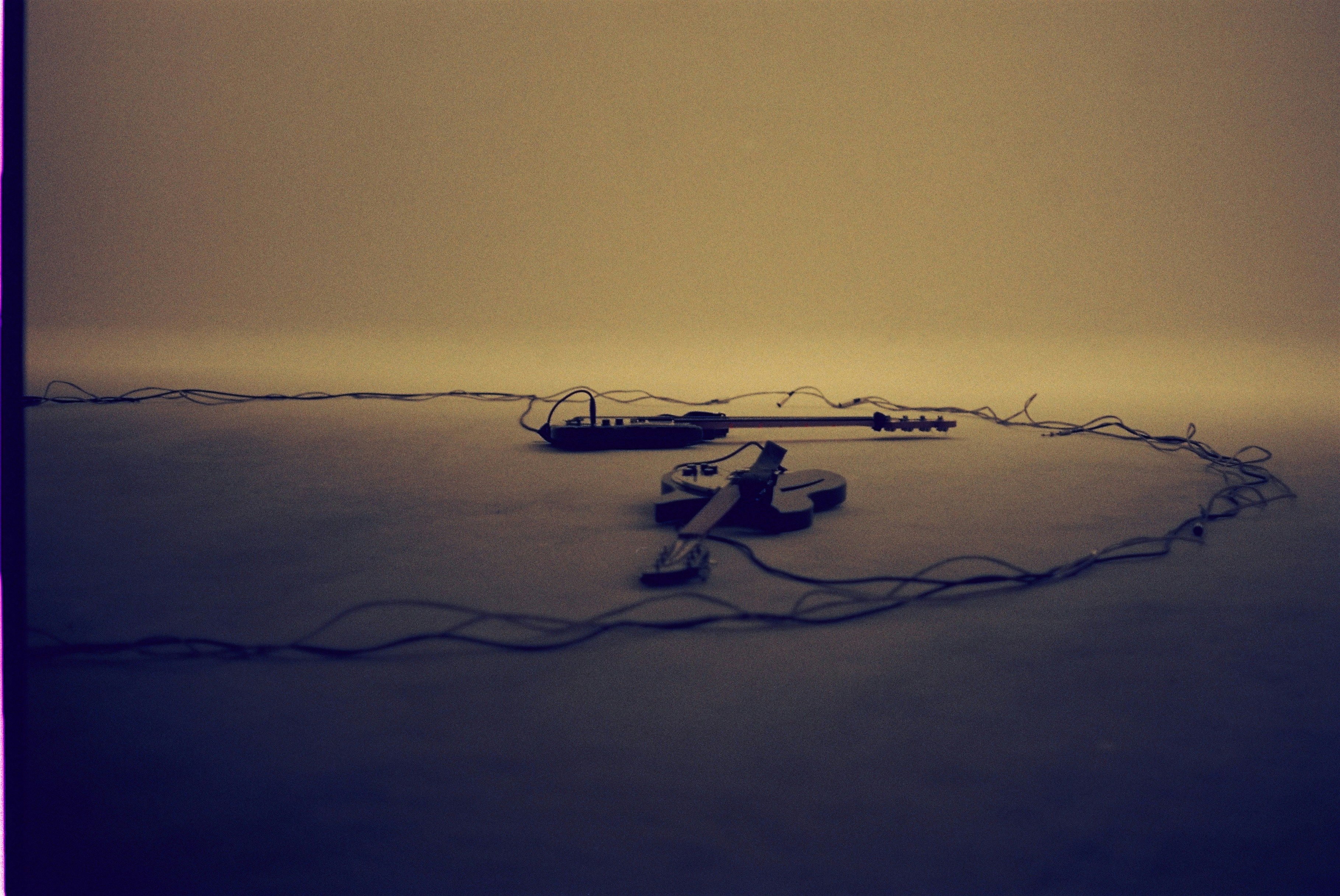 A guitar and amplifier lie on a sandy surface.