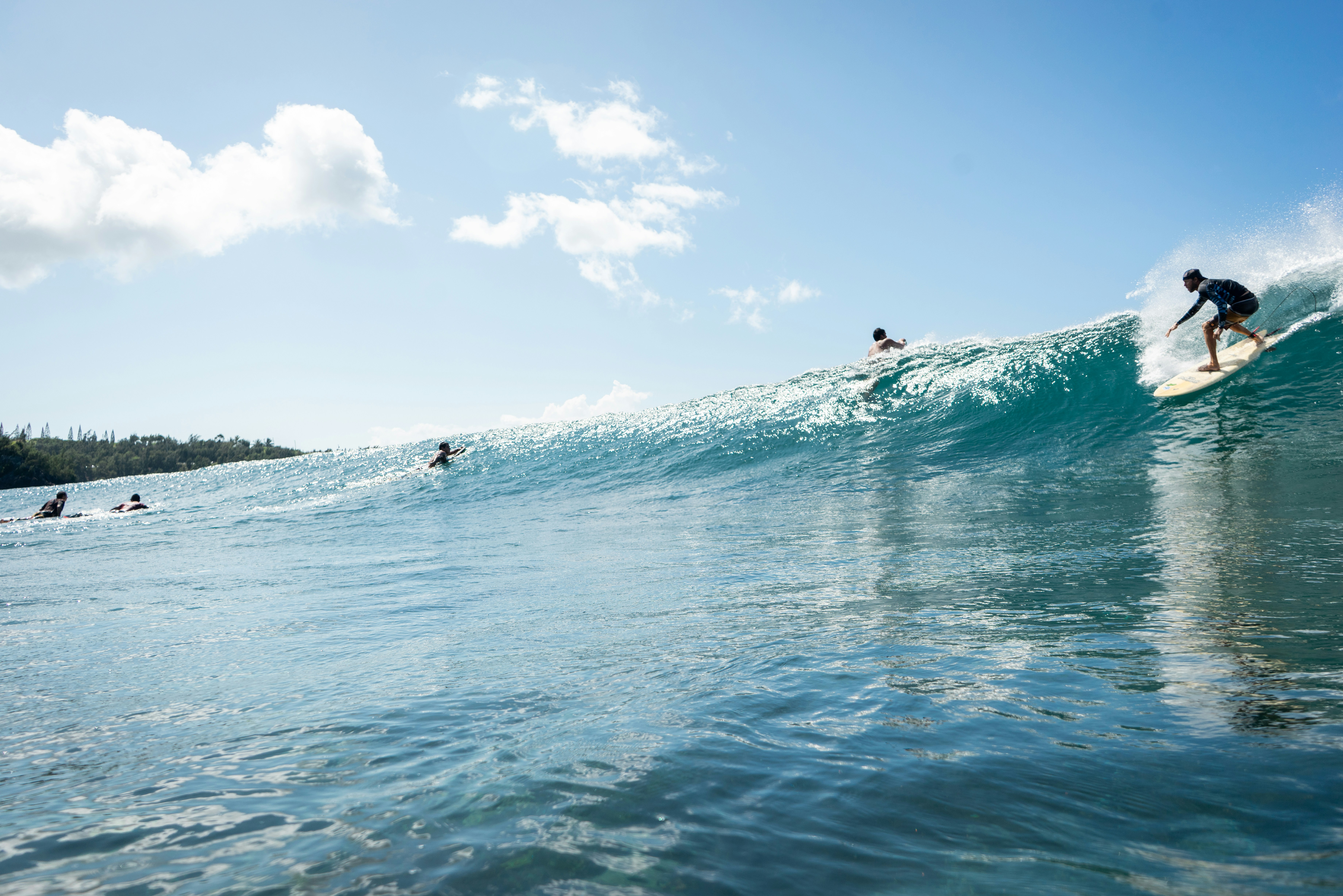 Surfers riding a large wave under a clear blue sky